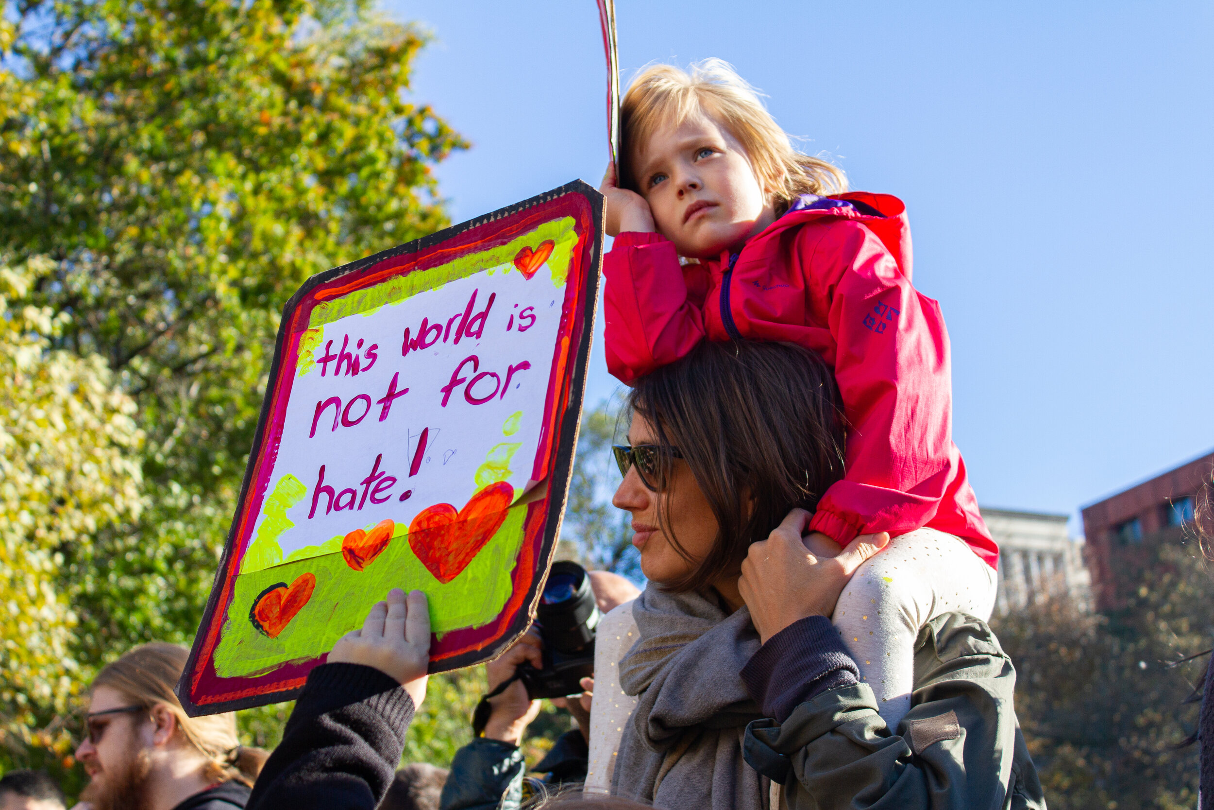 Young girl on her mother's shoulders, behind a sign, reading "this world is not for hate!" during a Love Rally in Washington Square Park | 2016