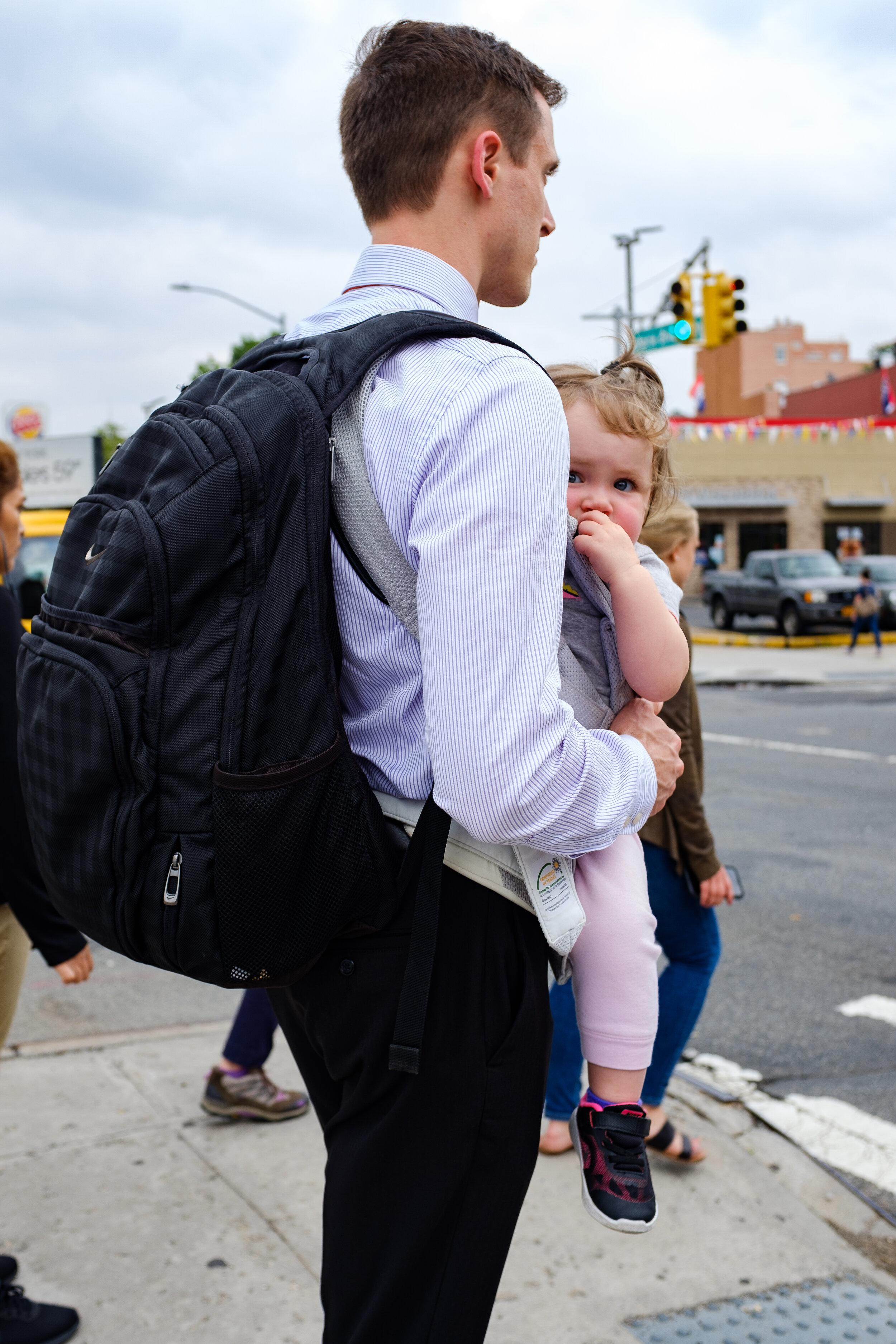 A man carrying his child in a baby carrier in Astoria, Queens | 2018