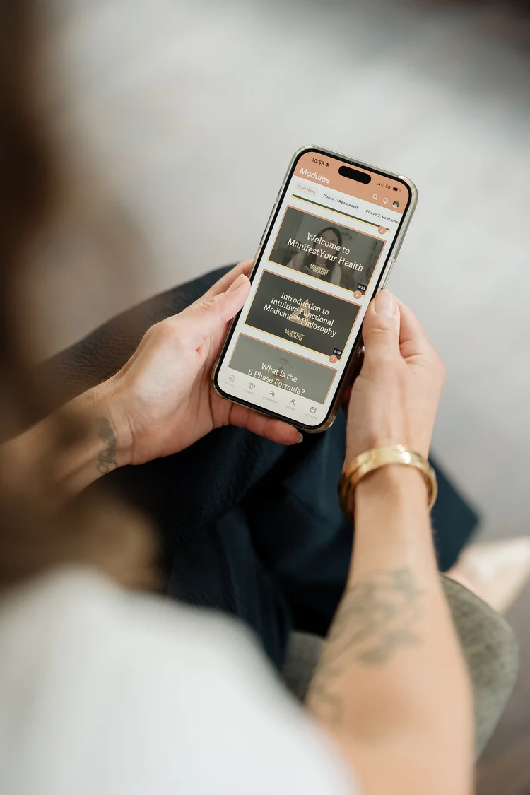 Person holding a smartphone open to the Manifest Your Health app, showing the course platform