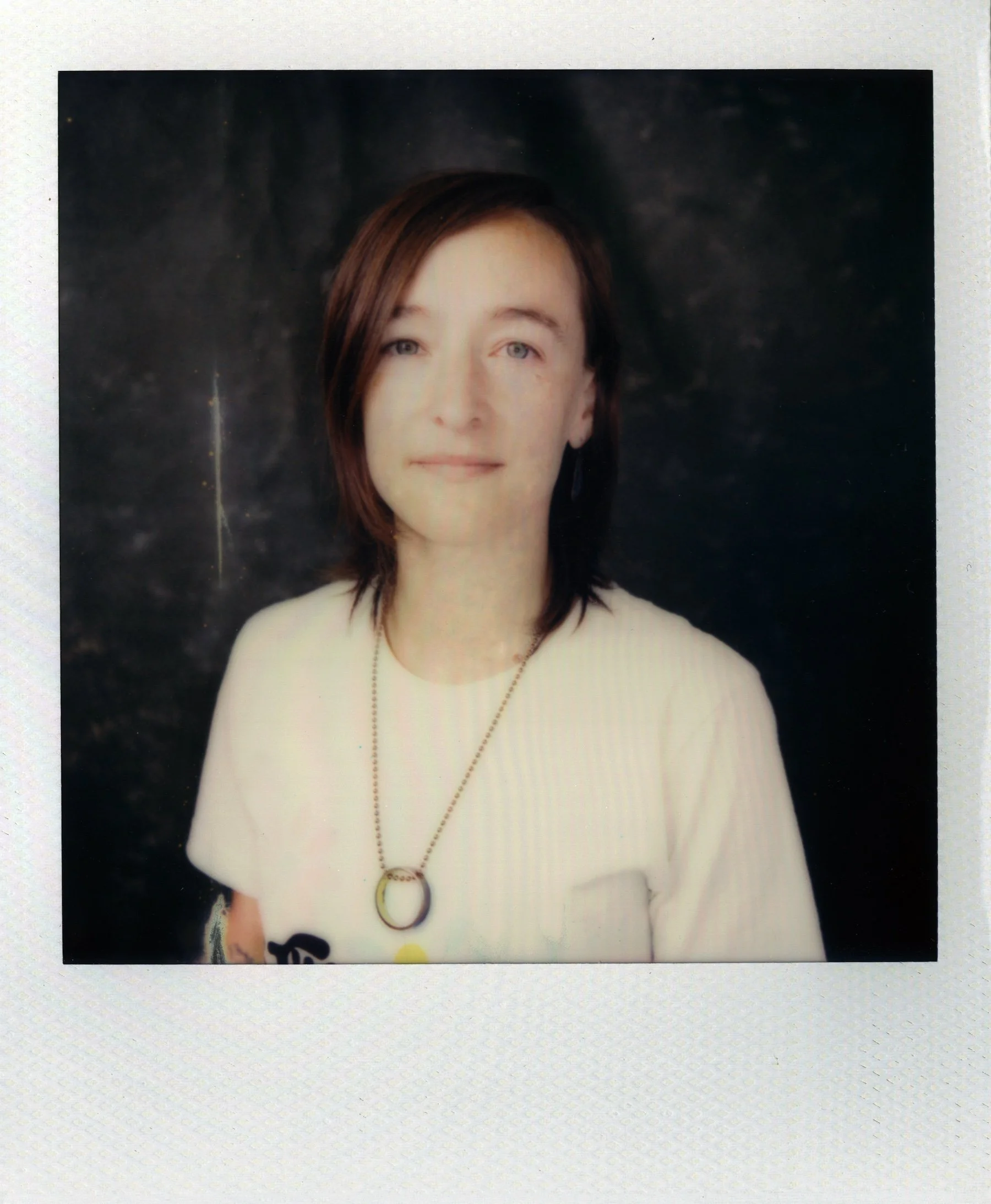A Polaroid portrait shows Sarah wearing a beige t-shirt and gold necklace with a large gold circle, looking straight into the camera.