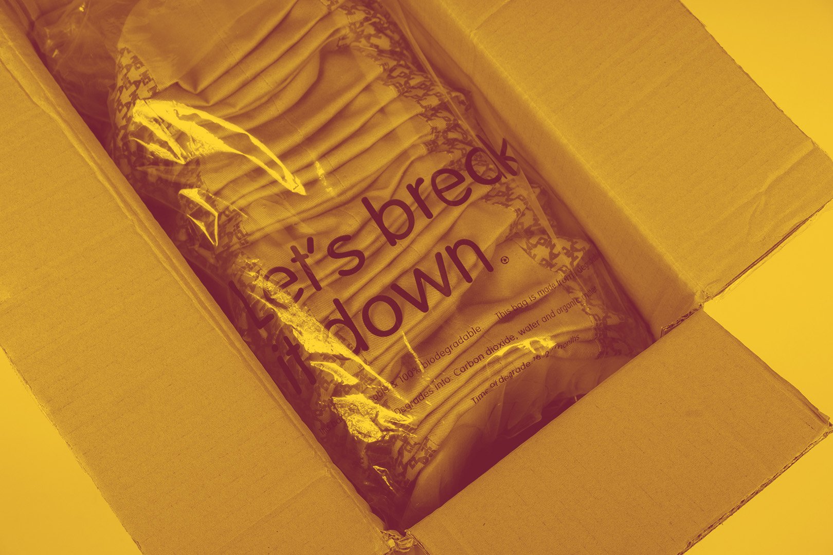 A cardboard box containing a sealed plastic bag of paper straws labeled "Let's break it down".