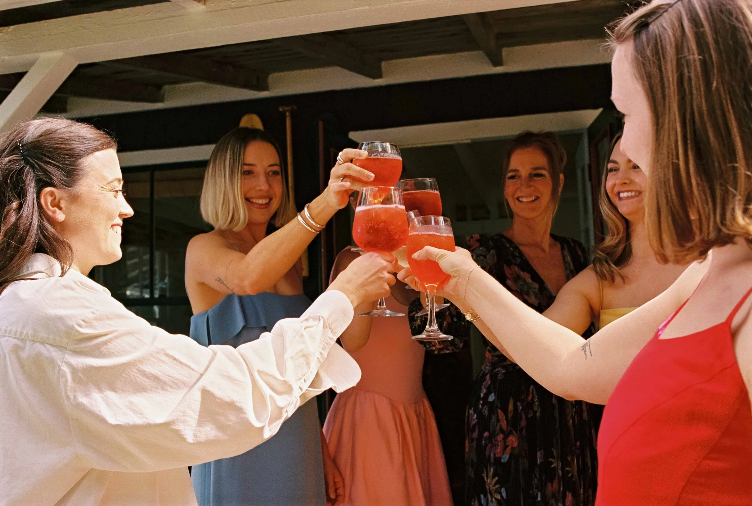 Bride and her bridesmaids doing a group cheers with drinks in Maine