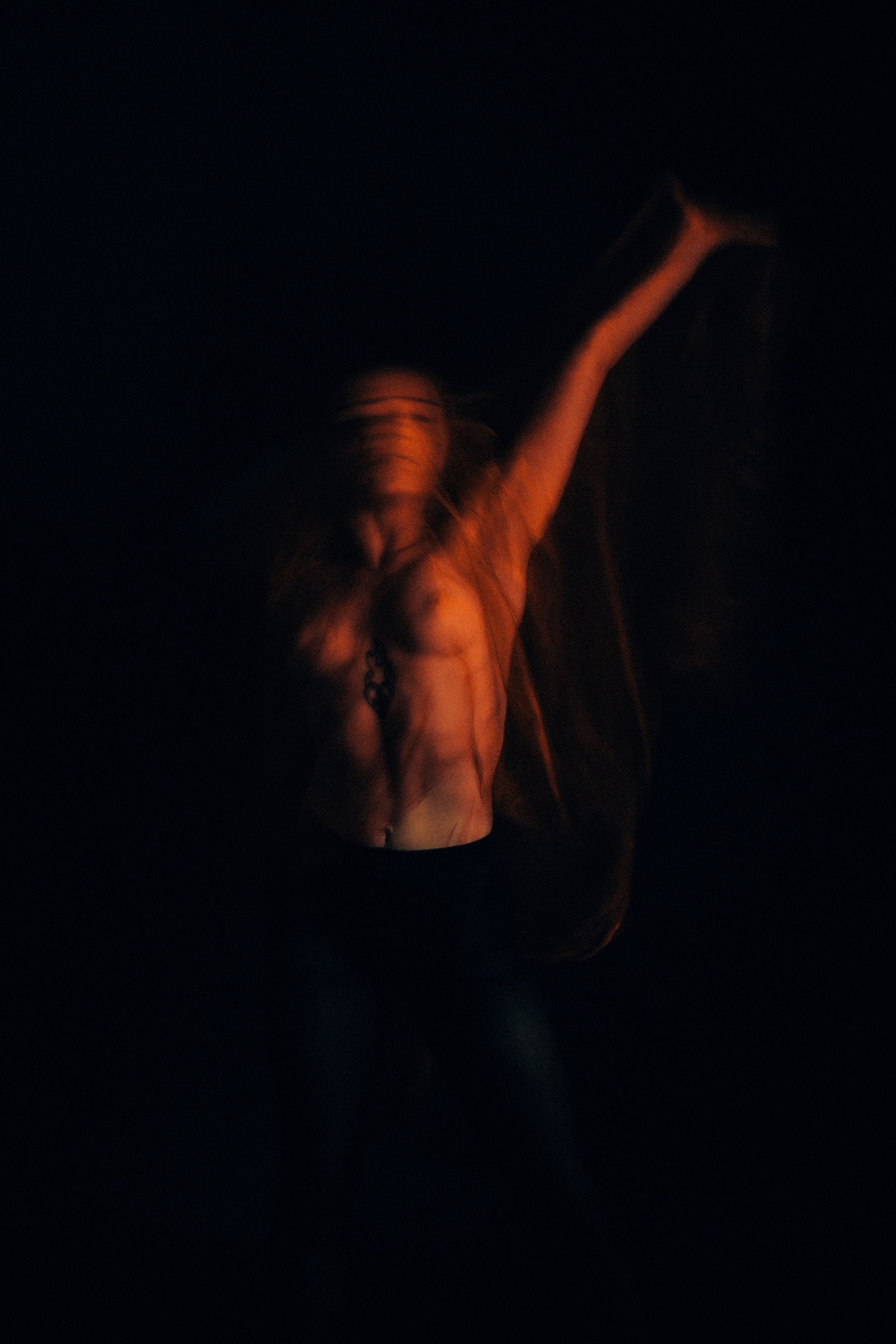 A person with long hair, possibly a woman, standing in a dark environment, illuminated by orange light.