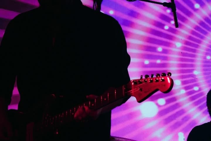 Person playing an electric guitar against a purple light display backdrop.