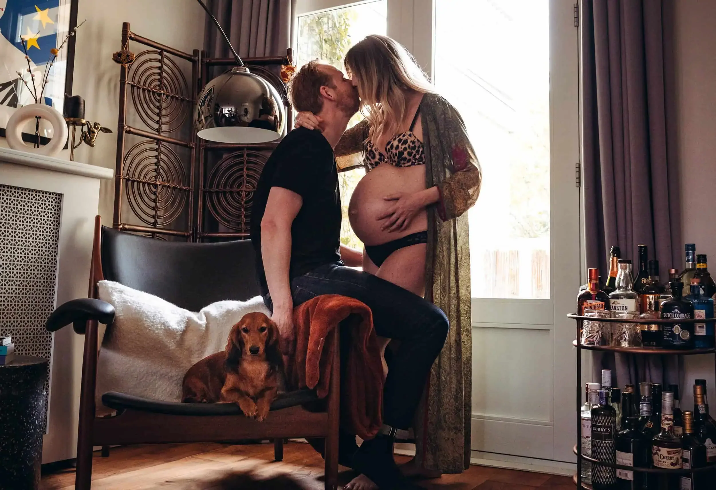Man with pregnant woman kissing and dog on sofa