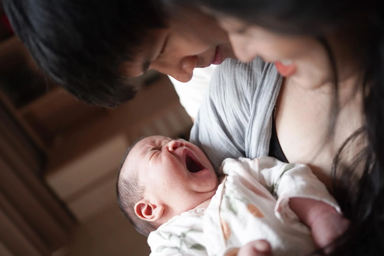 A mother holding her crying baby close, both leaning their heads towards each other.
