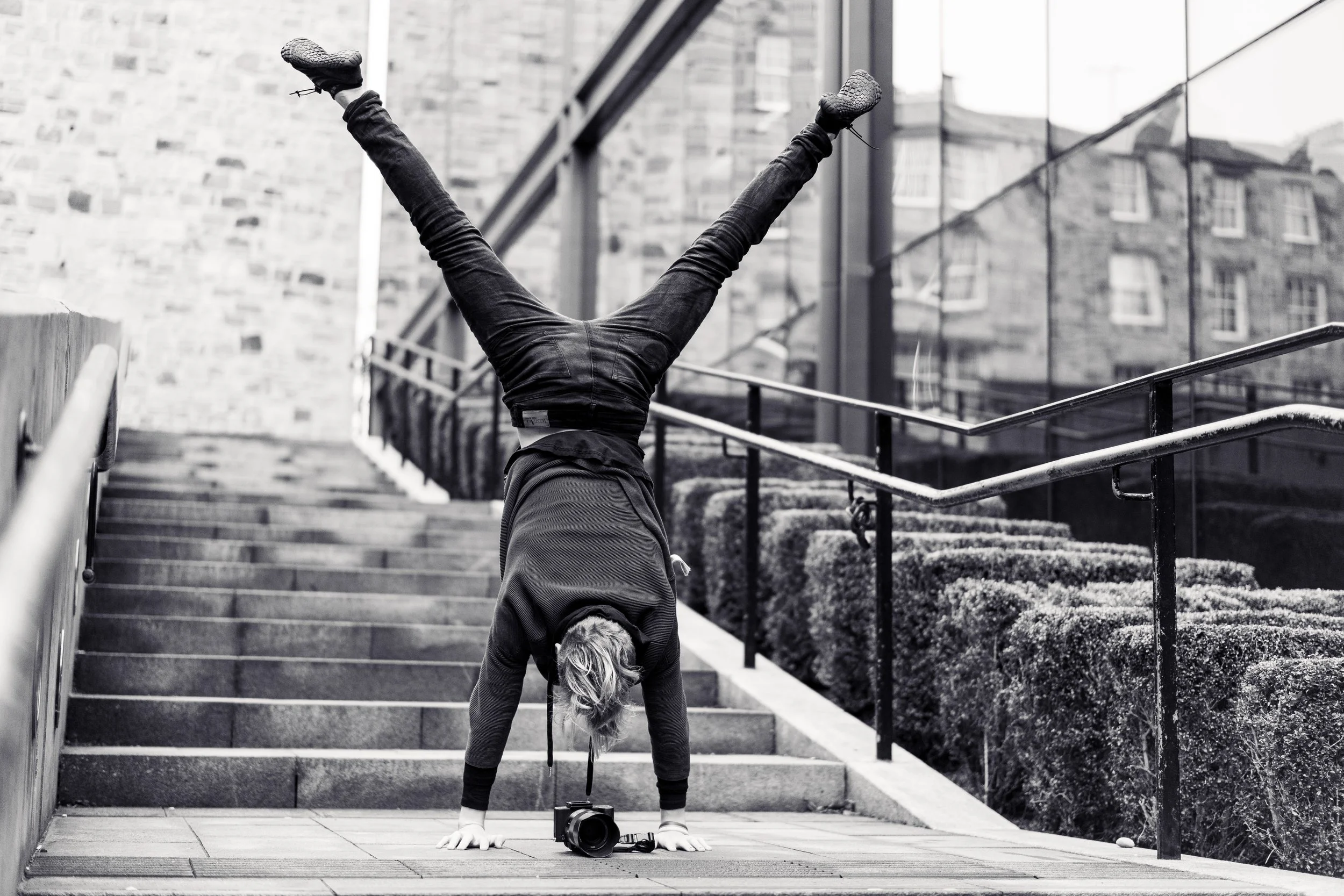 Person doing a handstand on stairs outdoors with a camera on the ground nearby