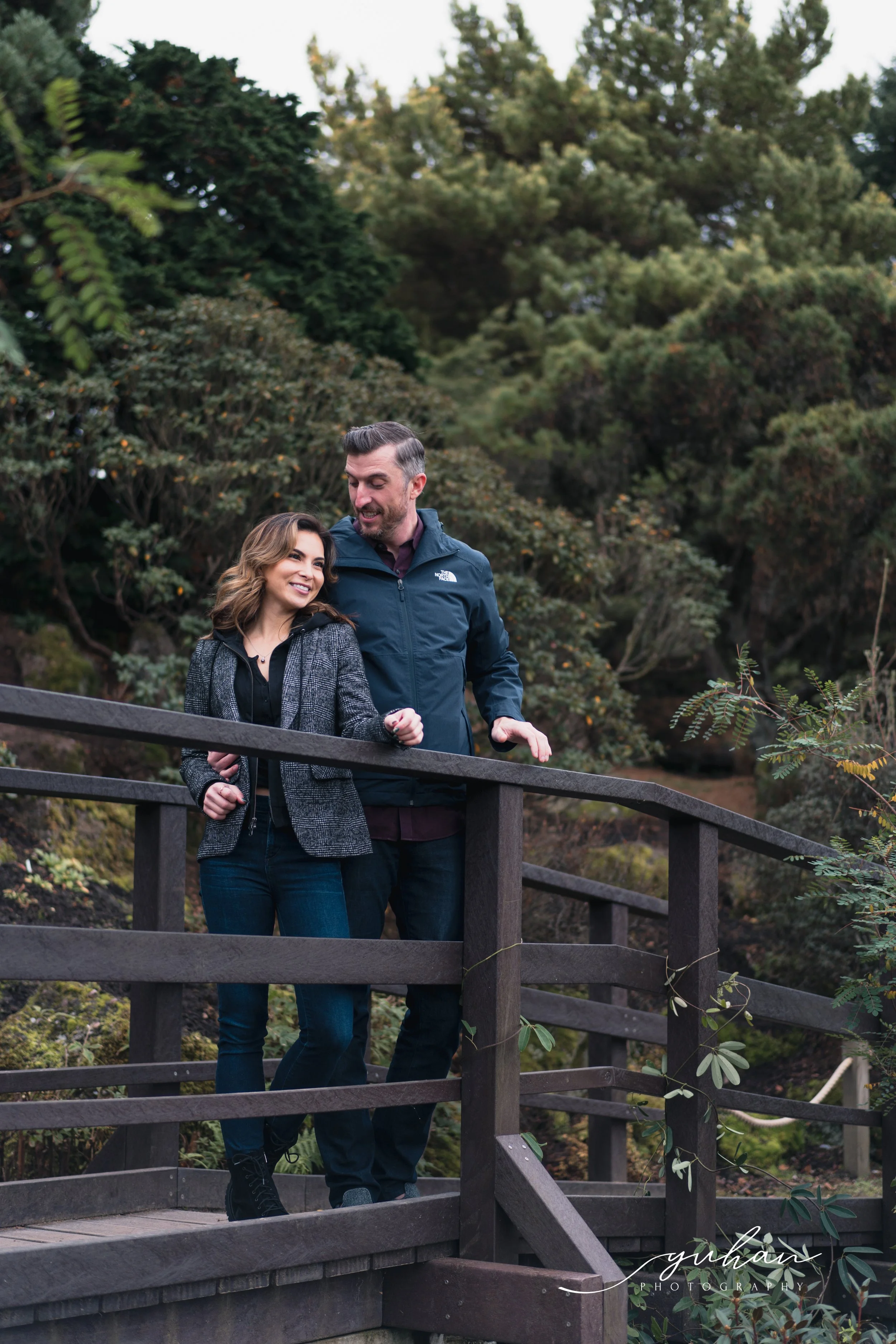 A man and woman walking together on a wooden bridge surrounded by trees.