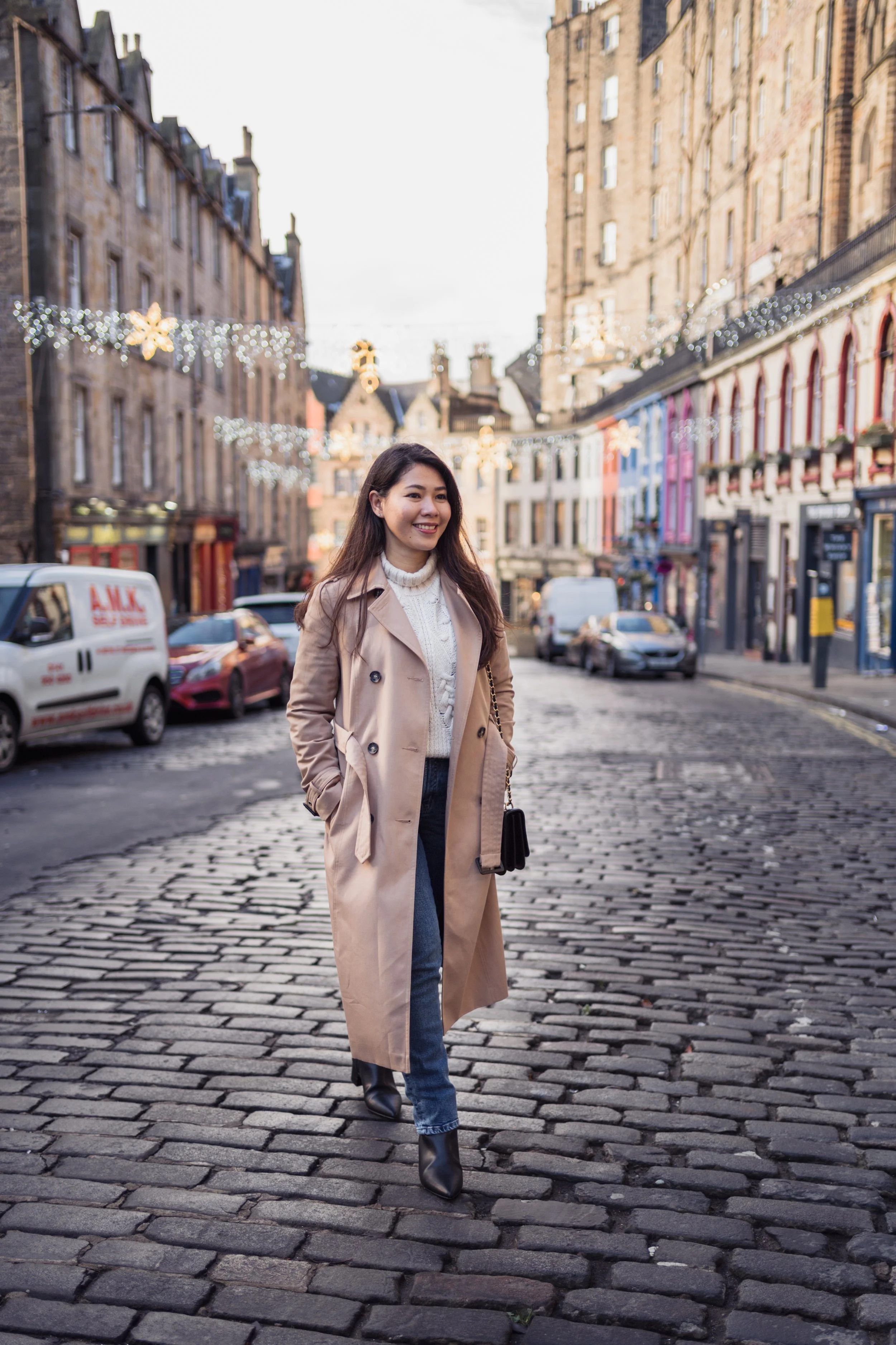 A woman walking on a cobblestone street in a city with decorated buildings and holiday lights.