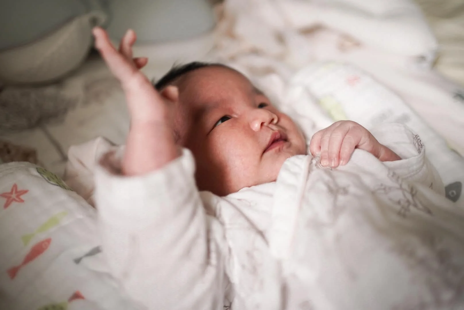 Close-up of a sleeping baby wearing a white patterned onesie, lying on a soft surface.