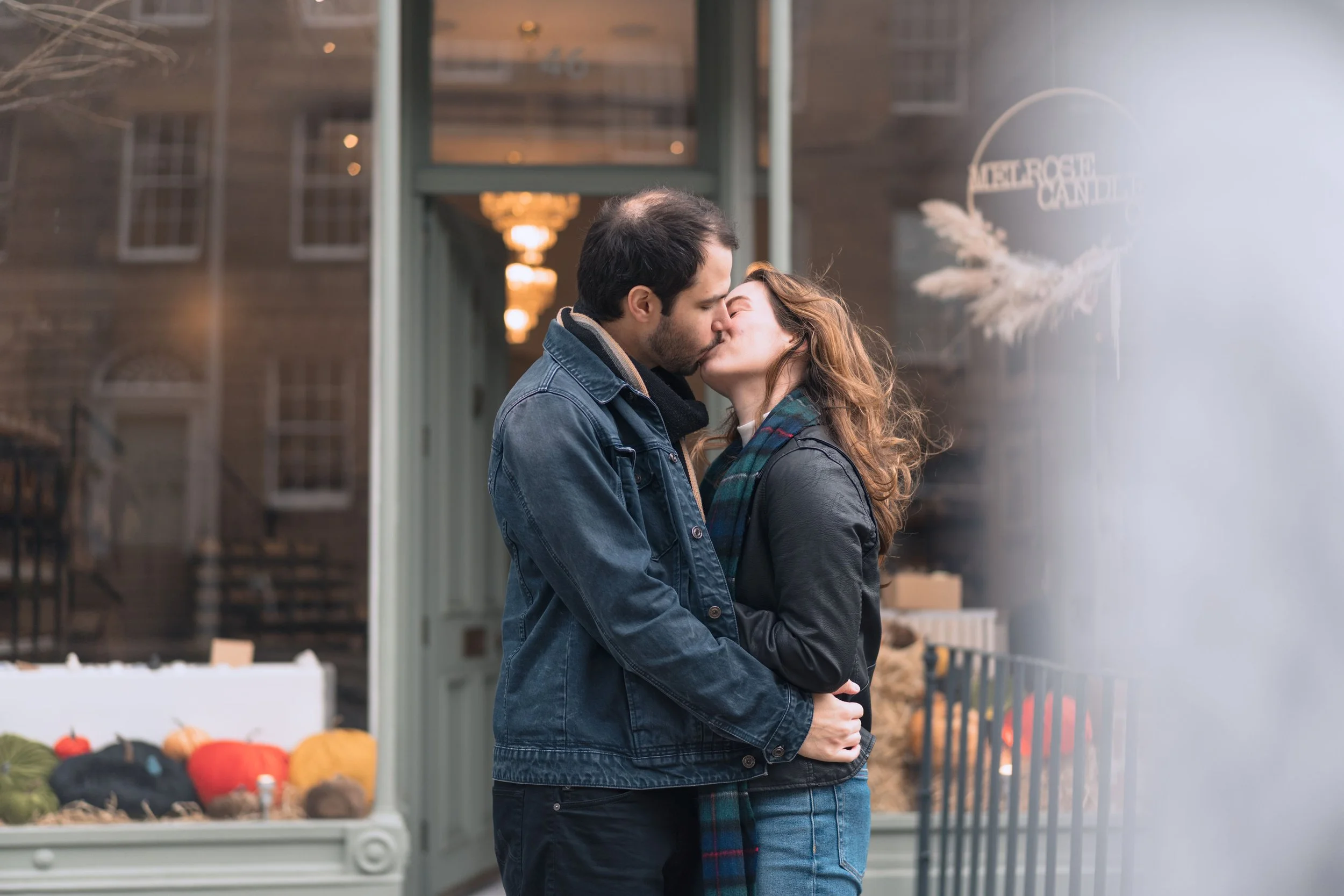 A couple sharing a kiss on a city street in front of a store with pumpkins and decorations.