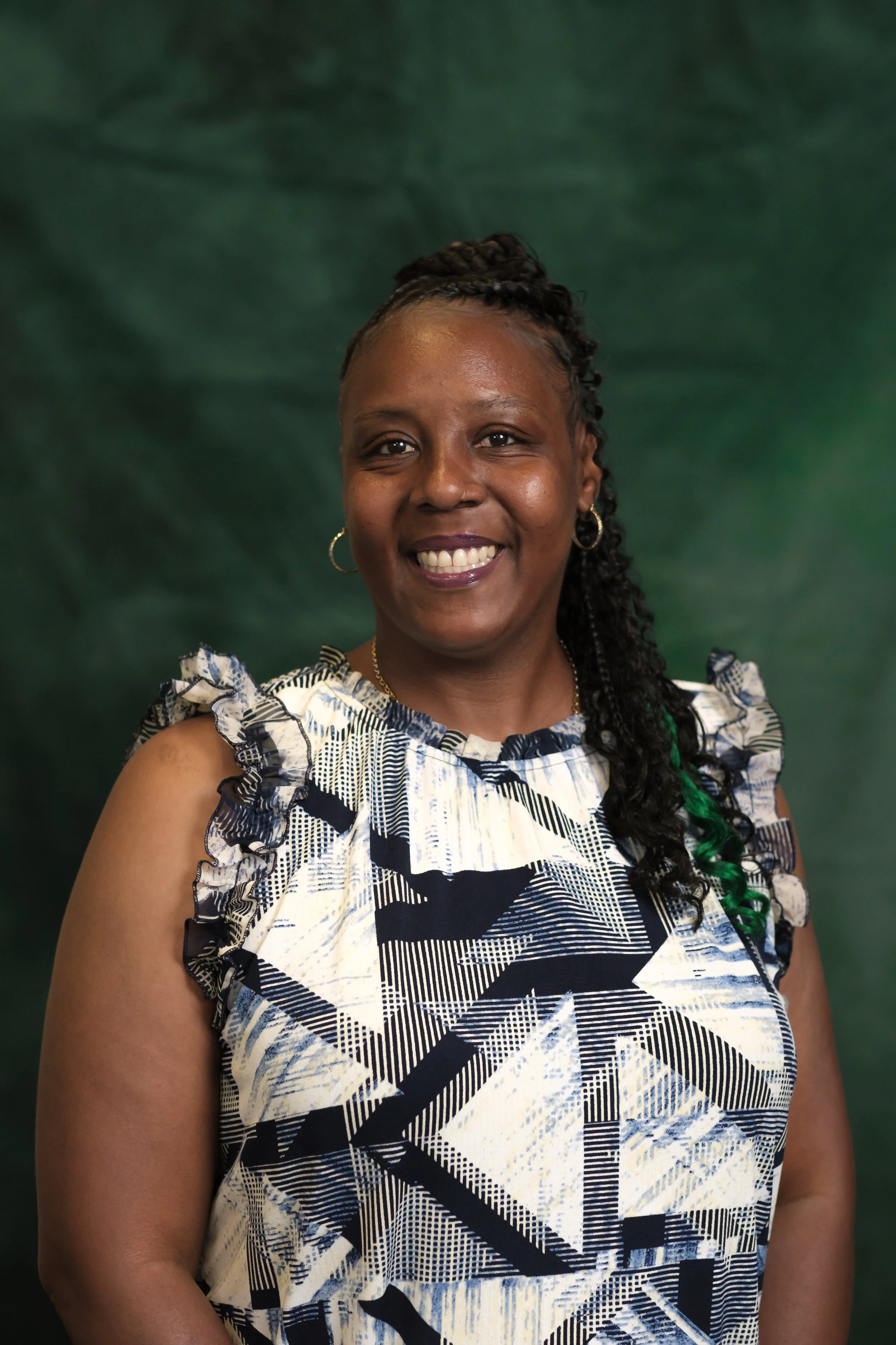A smiling woman wearing a green t-shirt with the words 'Diversion HKB' printed on it, standing against a green backdrop.