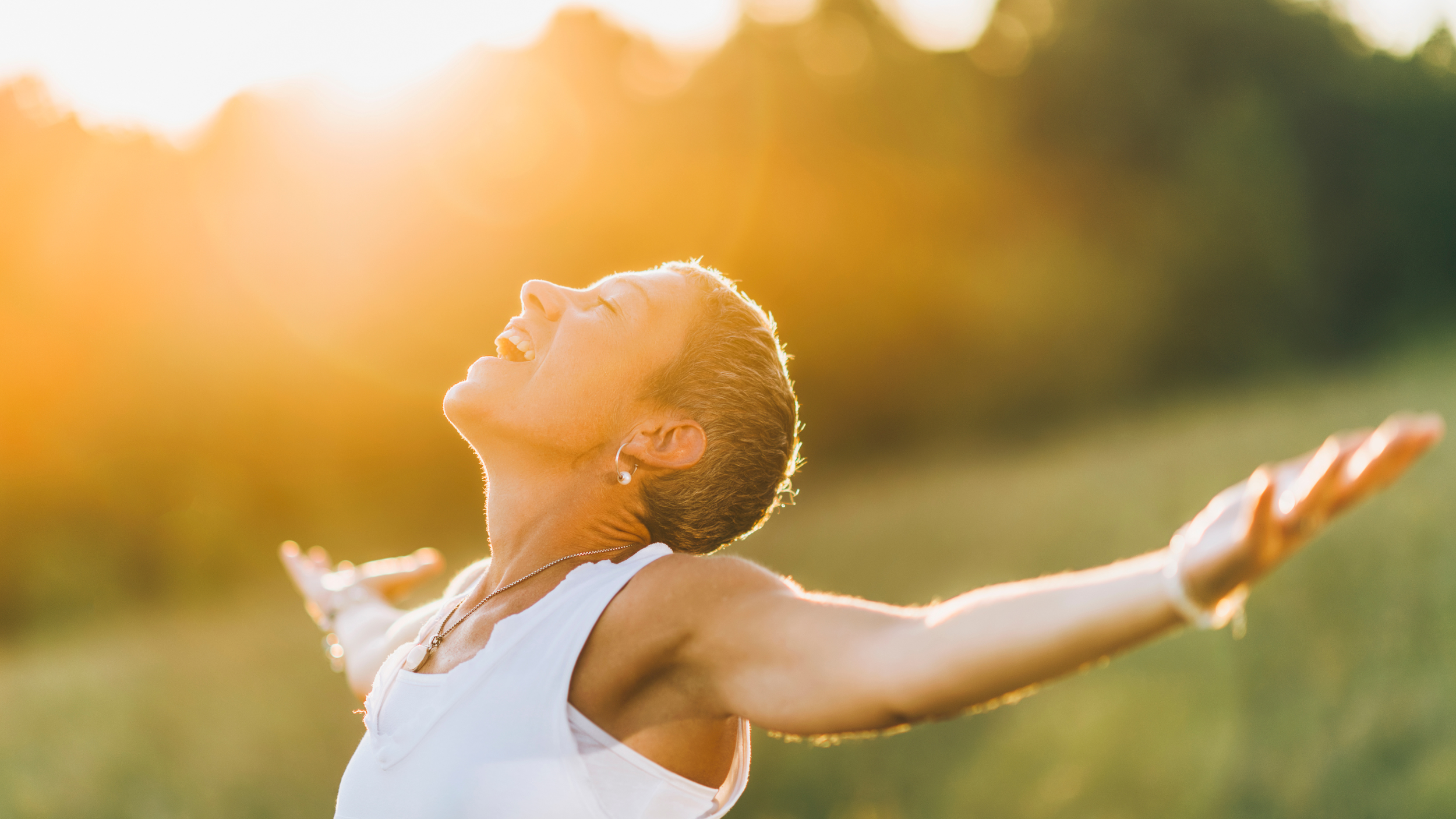 Mujer sonriendo con los brazos abiertos disfrutando al aire libre al atardecer