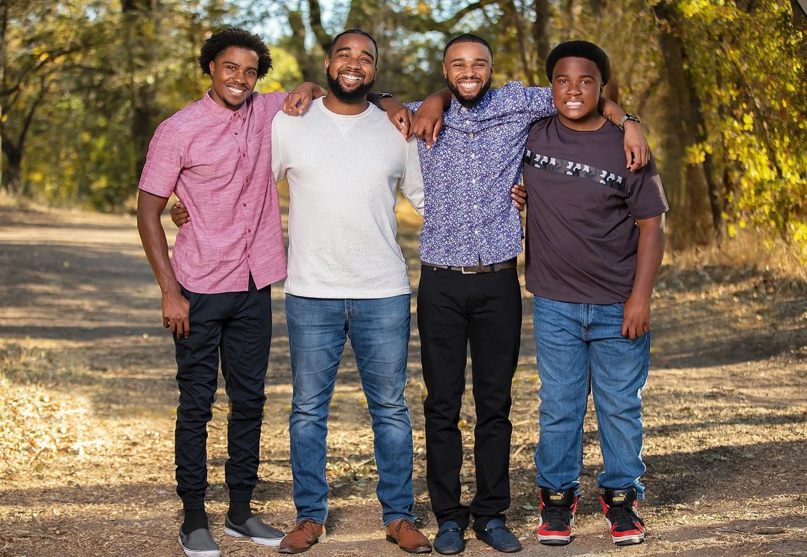 Four family members smiling with their arms around one another on a tree-lined outdoor path.