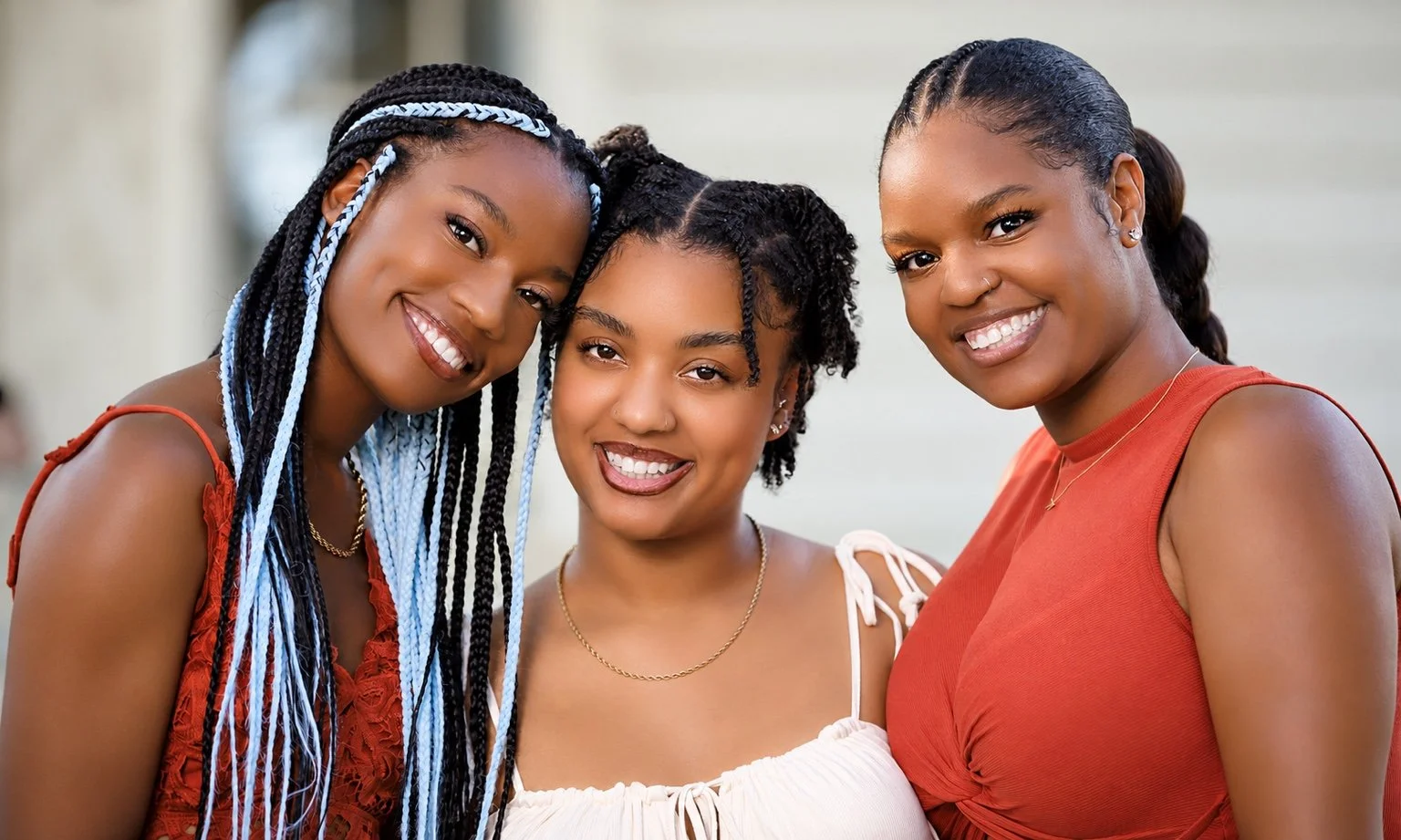 Three women smiling together in a close-up outdoor portrait, wearing red and white outfits.