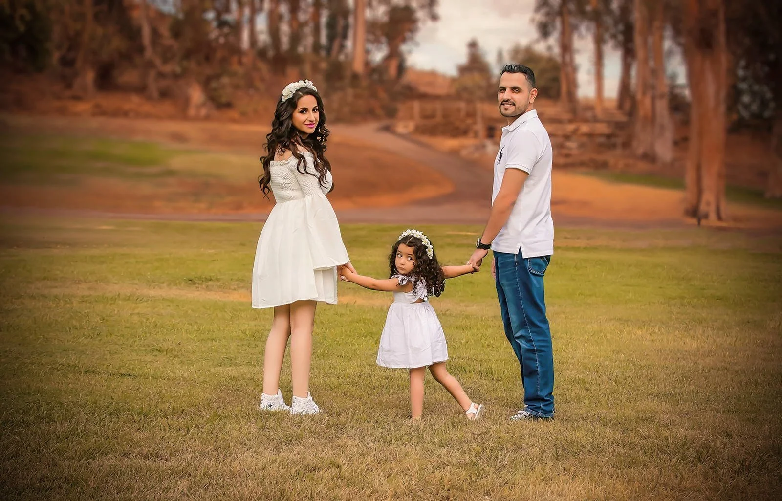 Parents holding hands with their young daughter during an outdoor family and maternity portrait session.