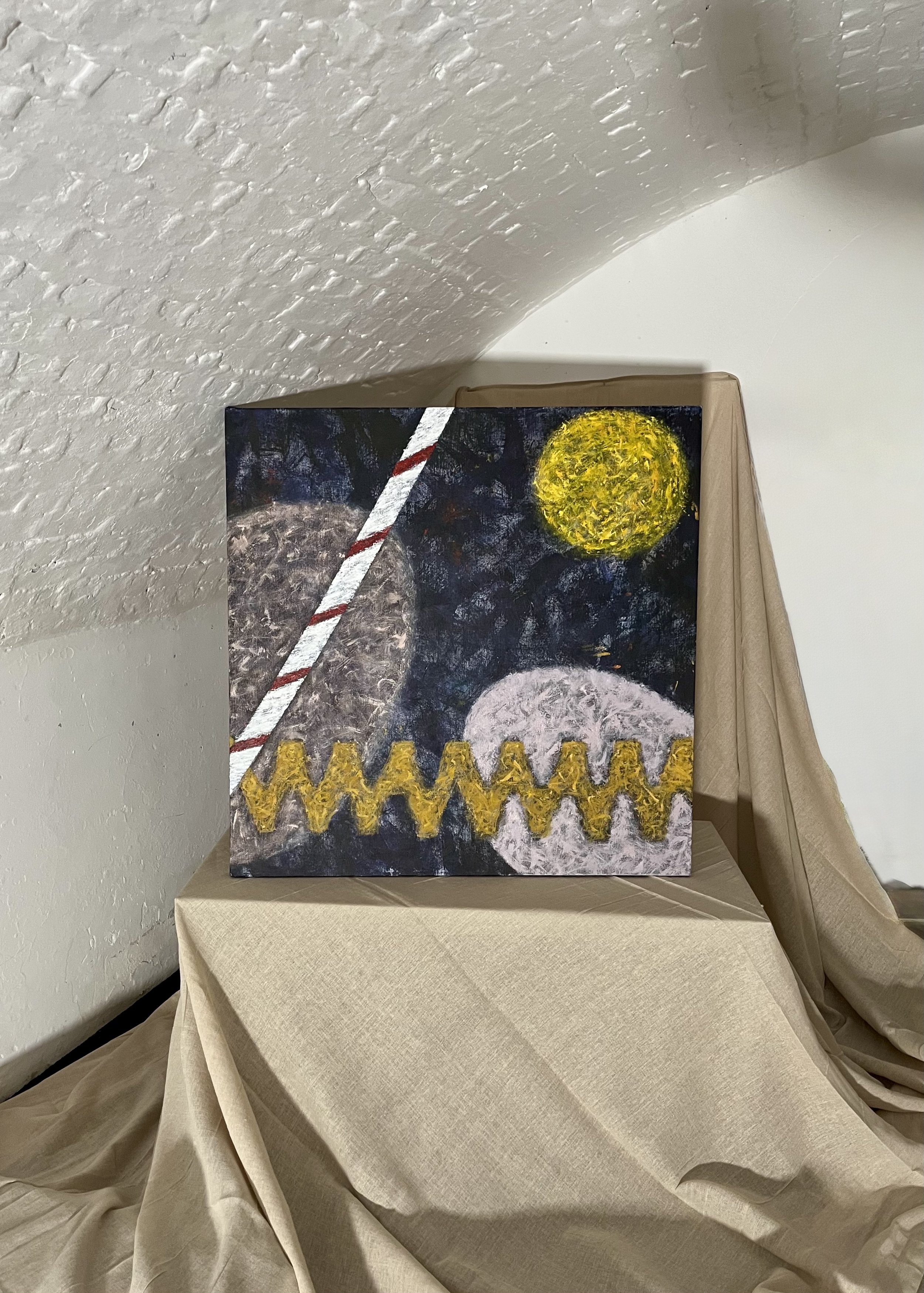 A small abstract painting on a canvas featuring a moon, sun, and zigzag pattern, placed on a draped beige cloth background.