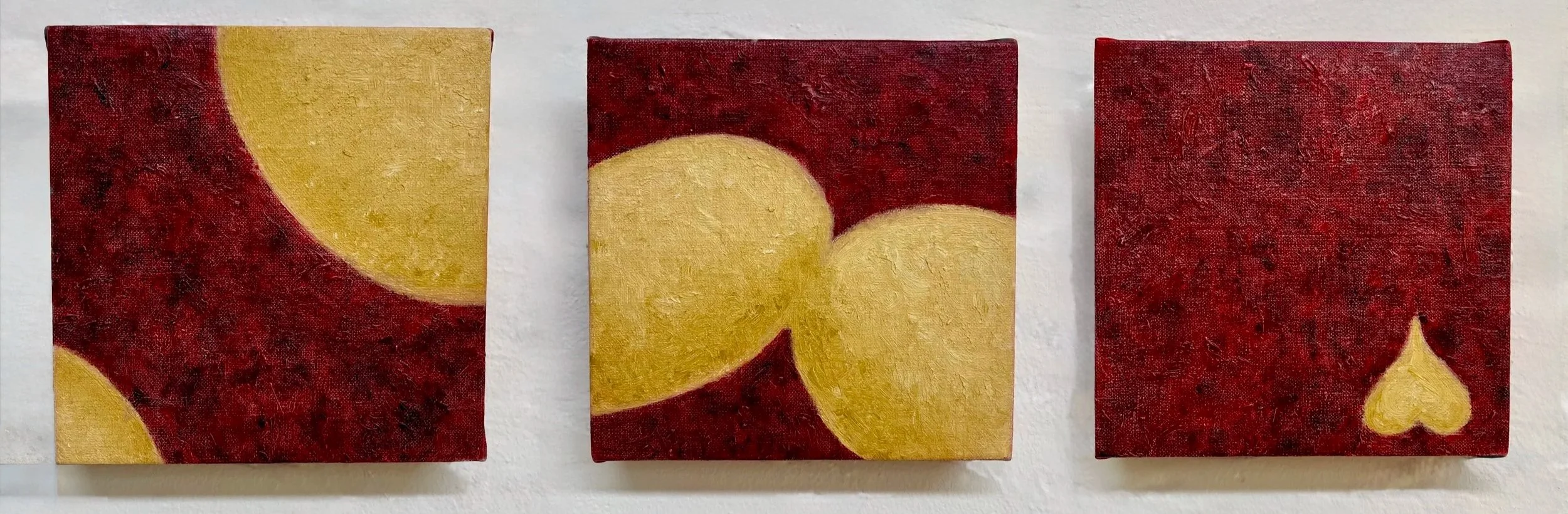 Three small abstract paintings featuring gold shapes against red backgrounds, arranged side by side on a wall.