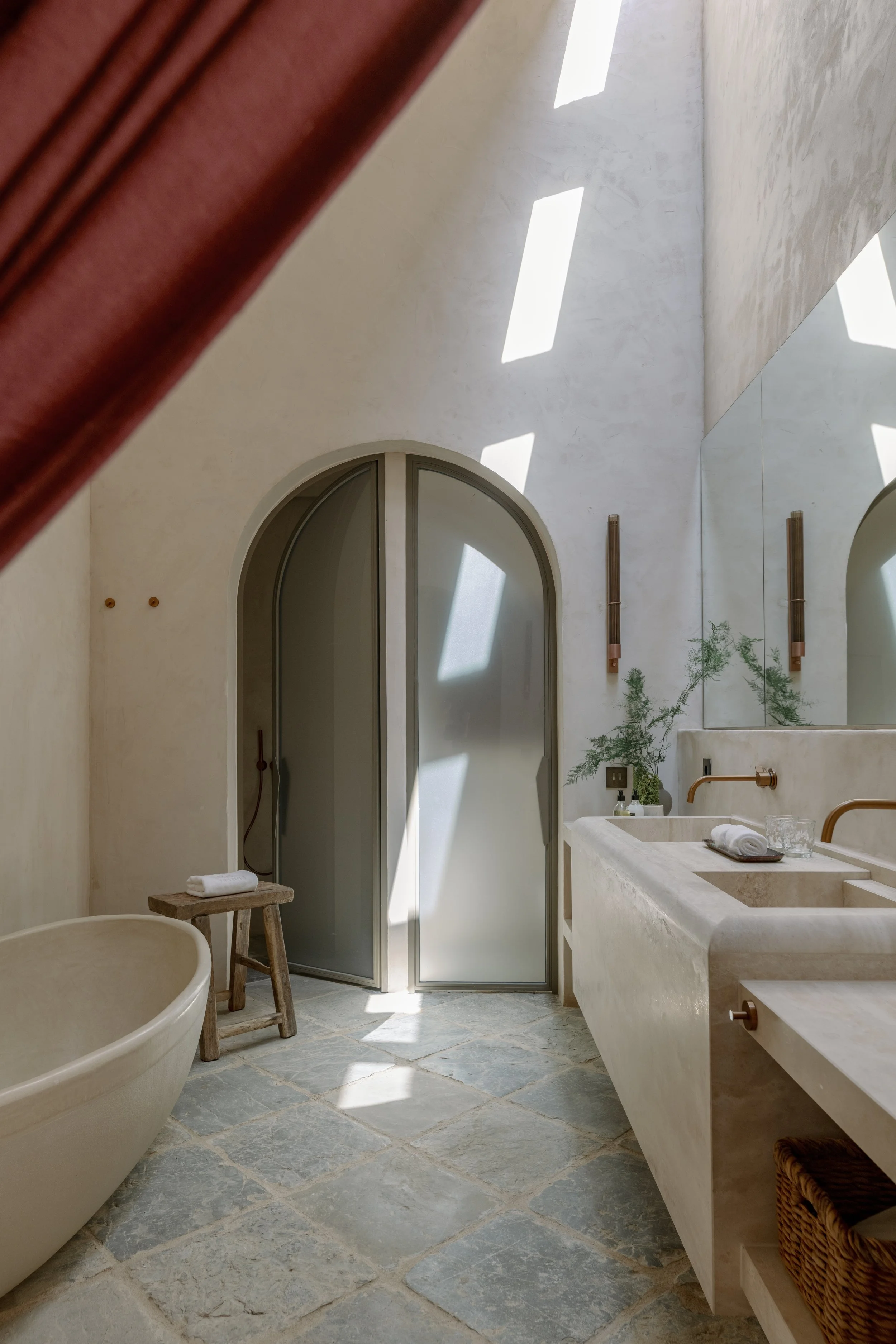 Interior of a modern bathroom with a stone floor, a freestanding bathtub, a double sink on a stone vanity, and sunlight streaming through skylights. Vestige Collection Son Ermita Binidufa Menorca Spain