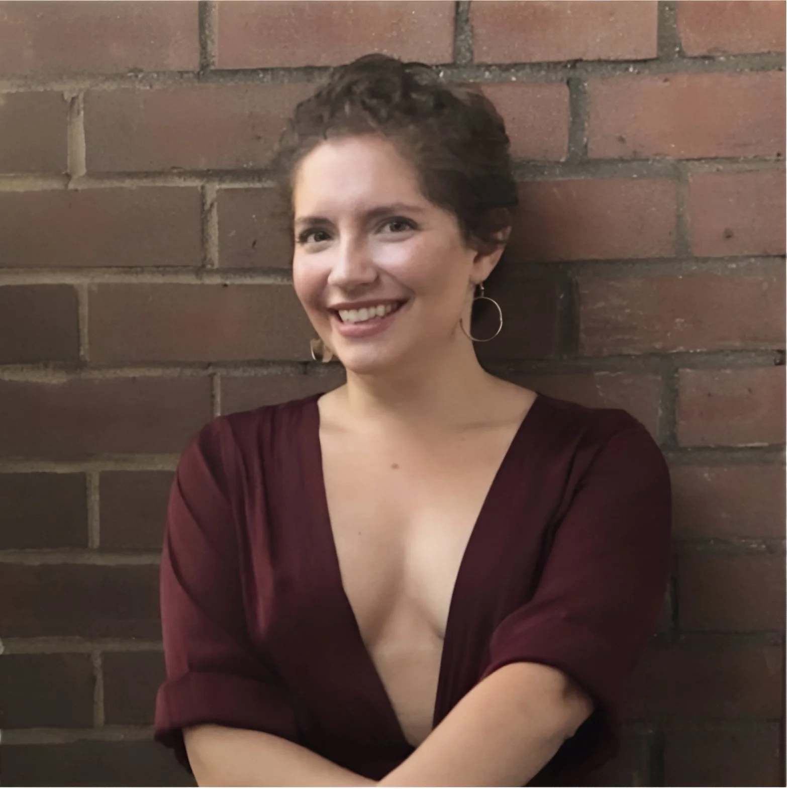 A portrait photo of Yael in a maroon top with a brick background.