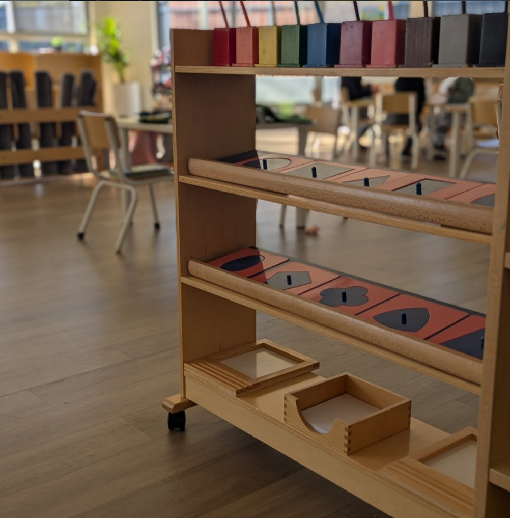 Wooden play cart with colorful blocks and game pieces inside a room with tables and chairs.