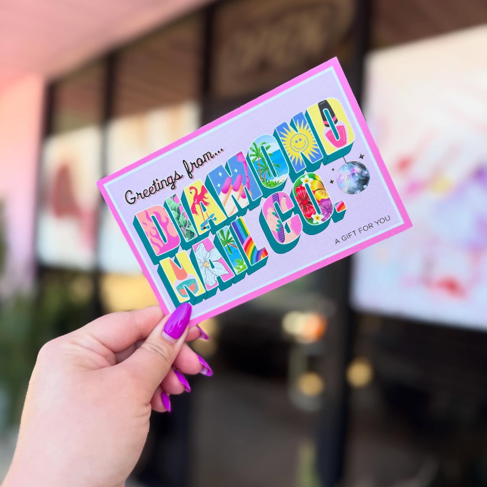 Close-up of a woman with bright pink painted nails holding a colorful greeting card with the word 'Holidays' and various festive illustrations.