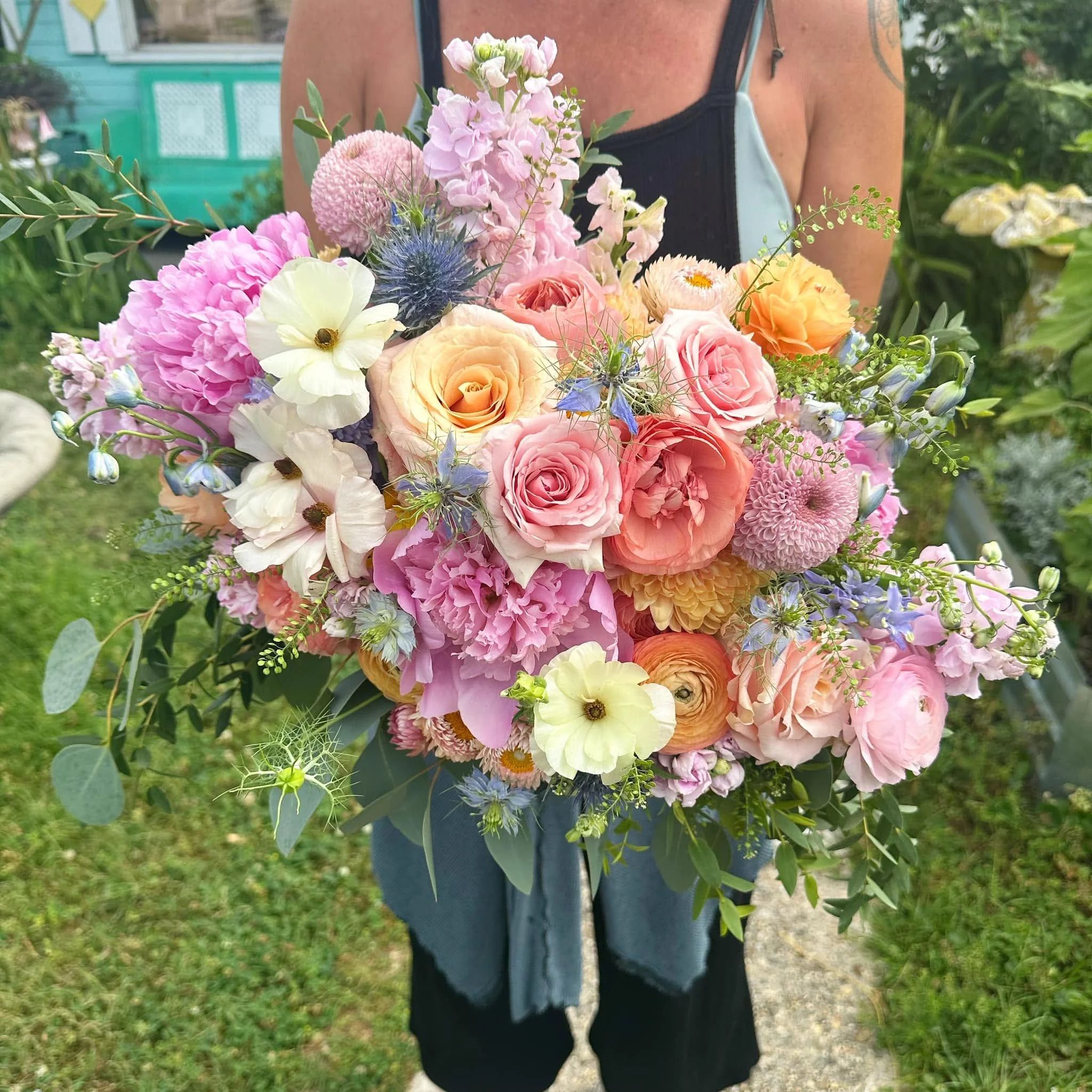 Person holding a large bouquet of pink, peach, and purple flowers outside in a garden.