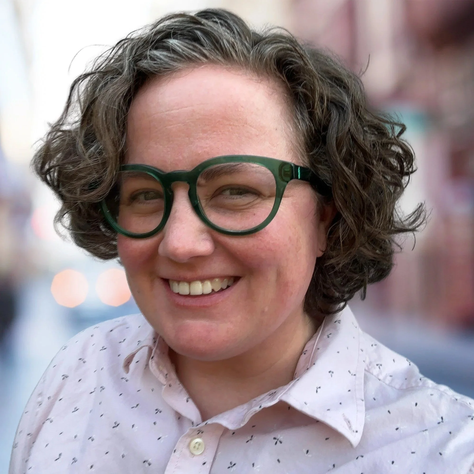 Close-up of smiling woman with glasses standing outdoors in an urban setting