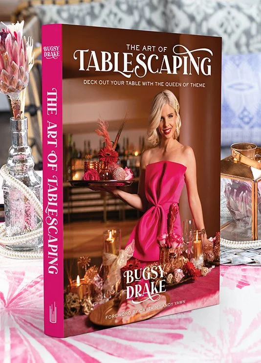 A hardcover copy of The Art of Tablescaping by Bugsy Drake stand on a decorated table
