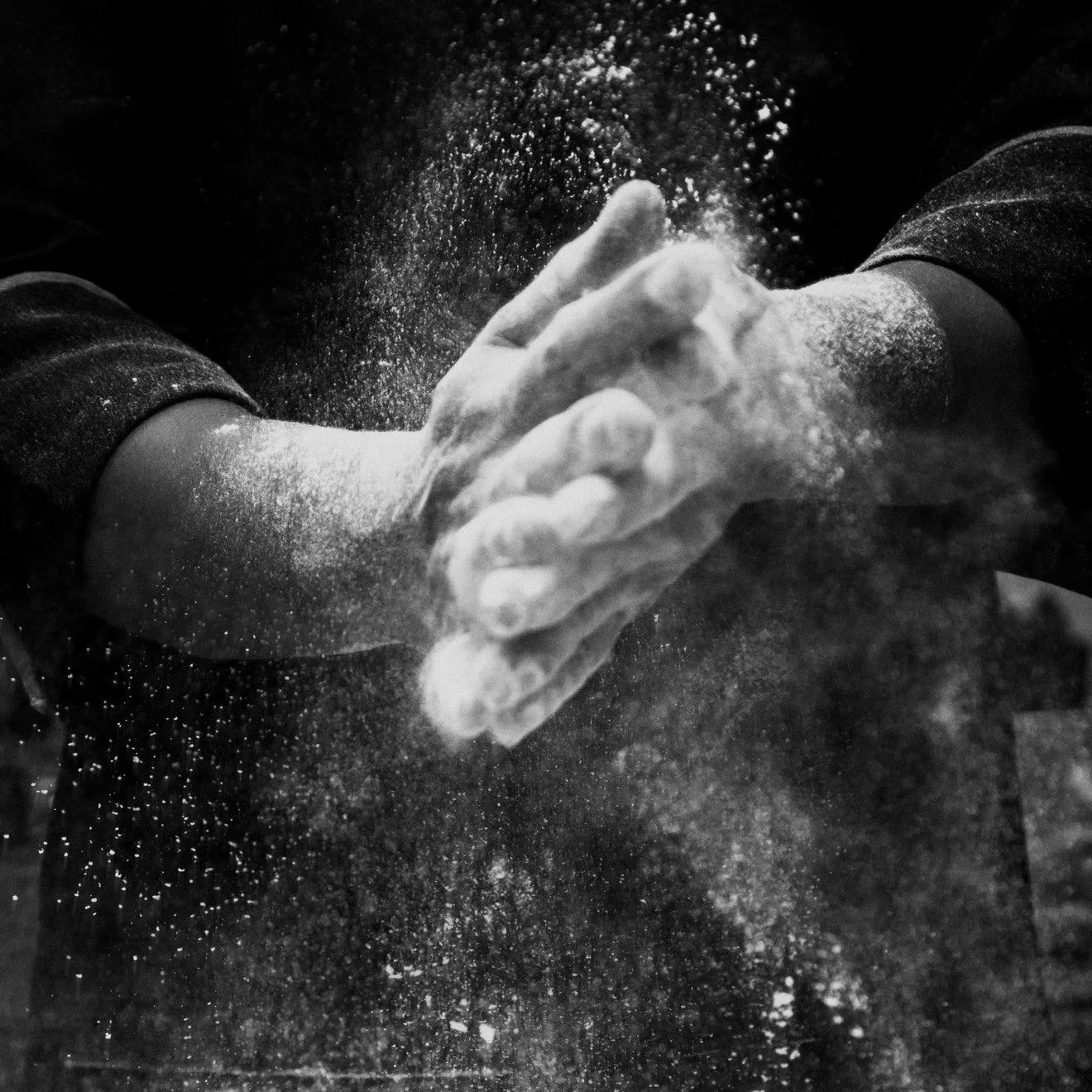 Person clapping hands with flour or powder flying in the air in black and white.