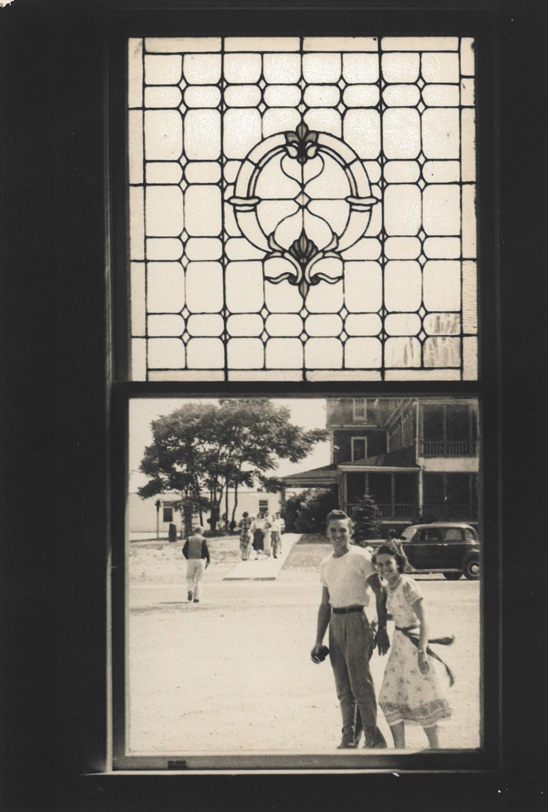 A black and white photograph of a stained glass window above a view of people walking outside a building.