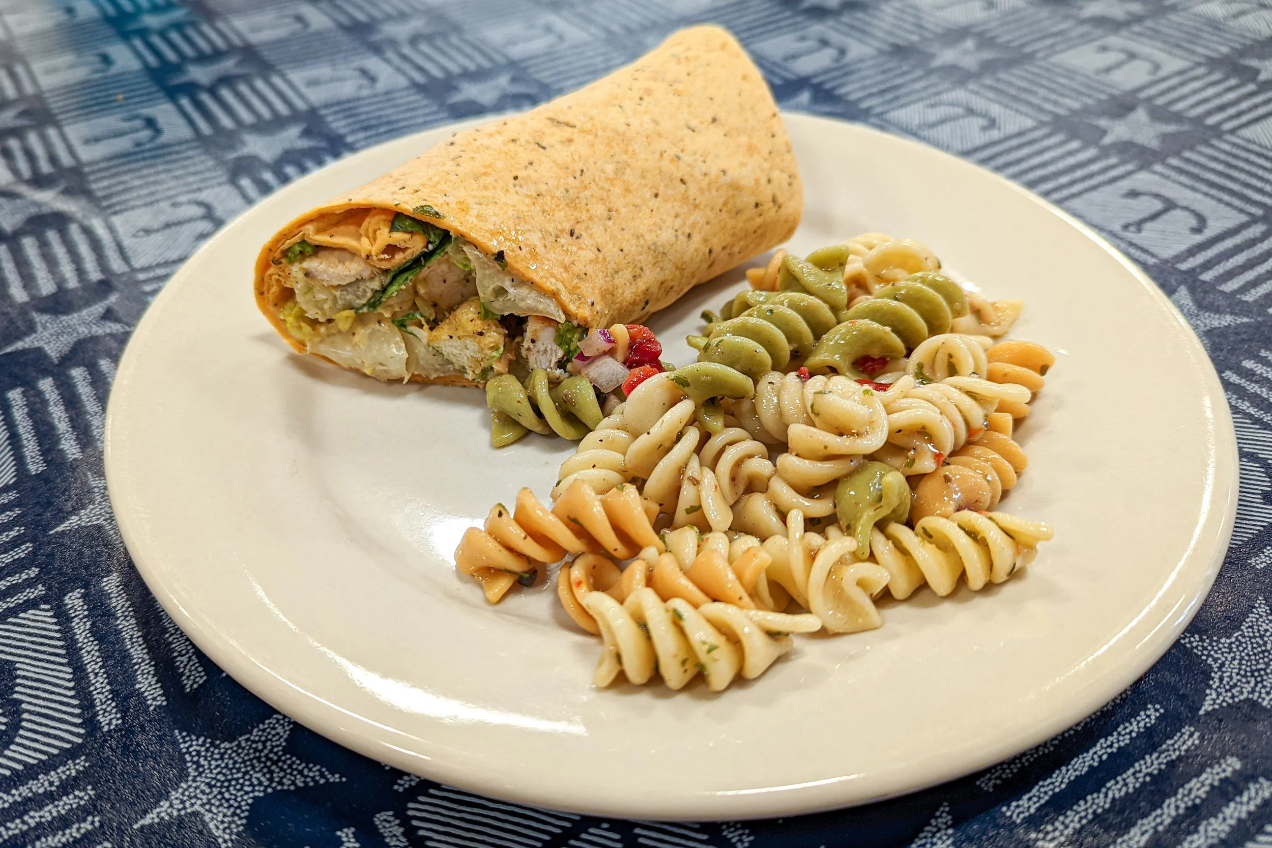 Plate with chicken wrap and tri-color rotini pasta salad on a blue patriotic tablecloth