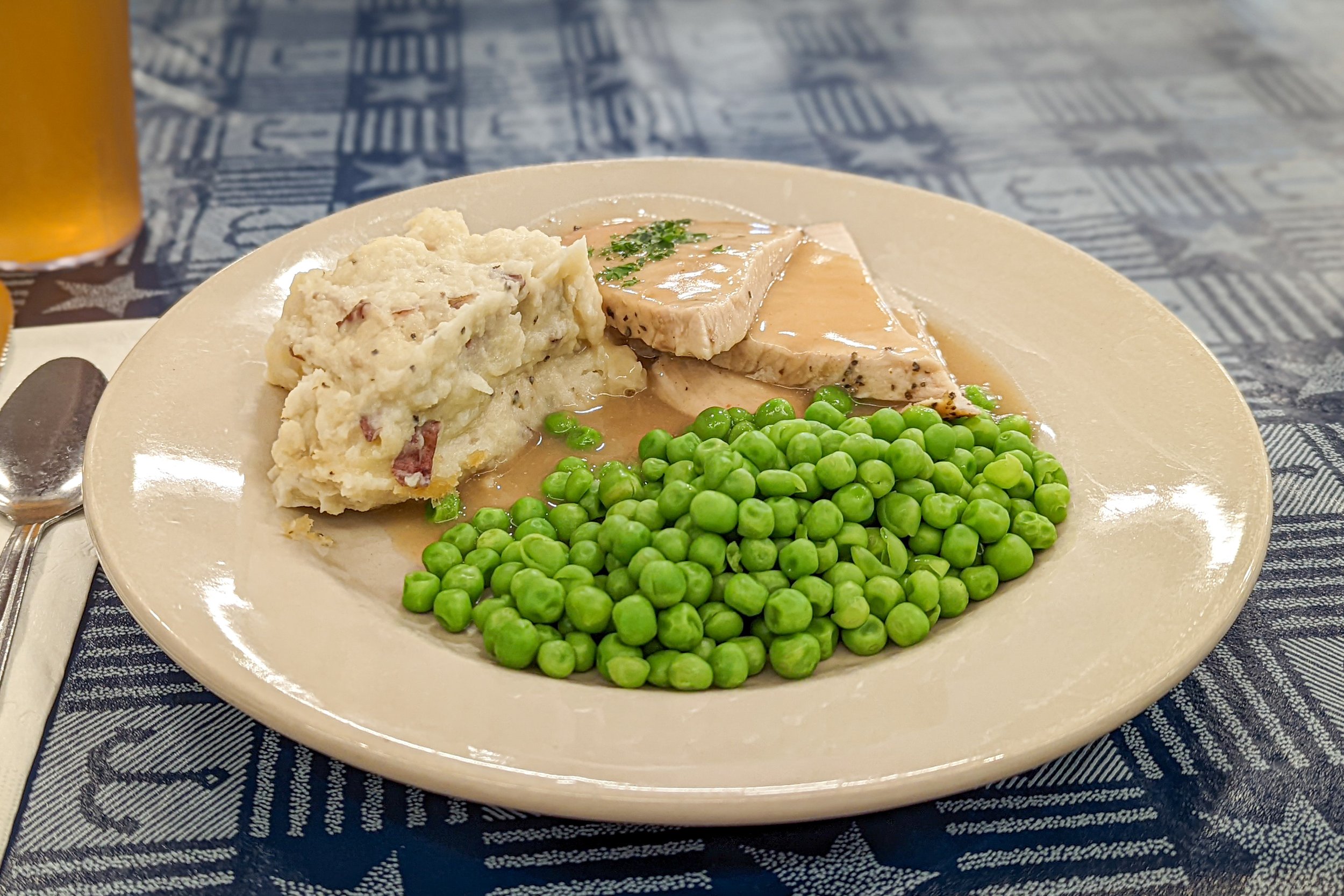 Plate of mashed potatoes with bacon bits, green peas, and slices of turkey with gravy.