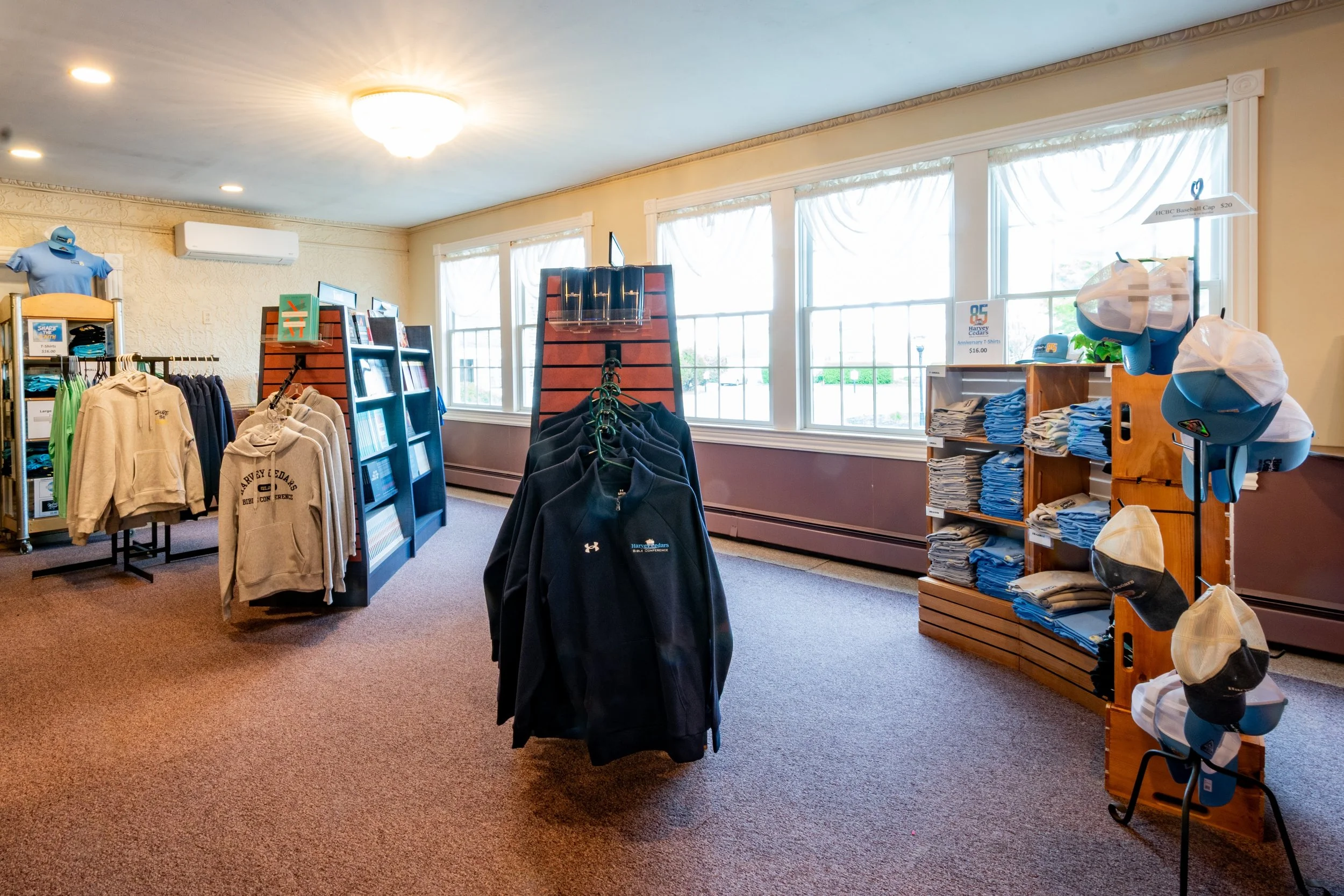 Interior of a retail store with shelves and racks displaying clothing and hats, large windows letting in natural light, and clothing accessories on display.