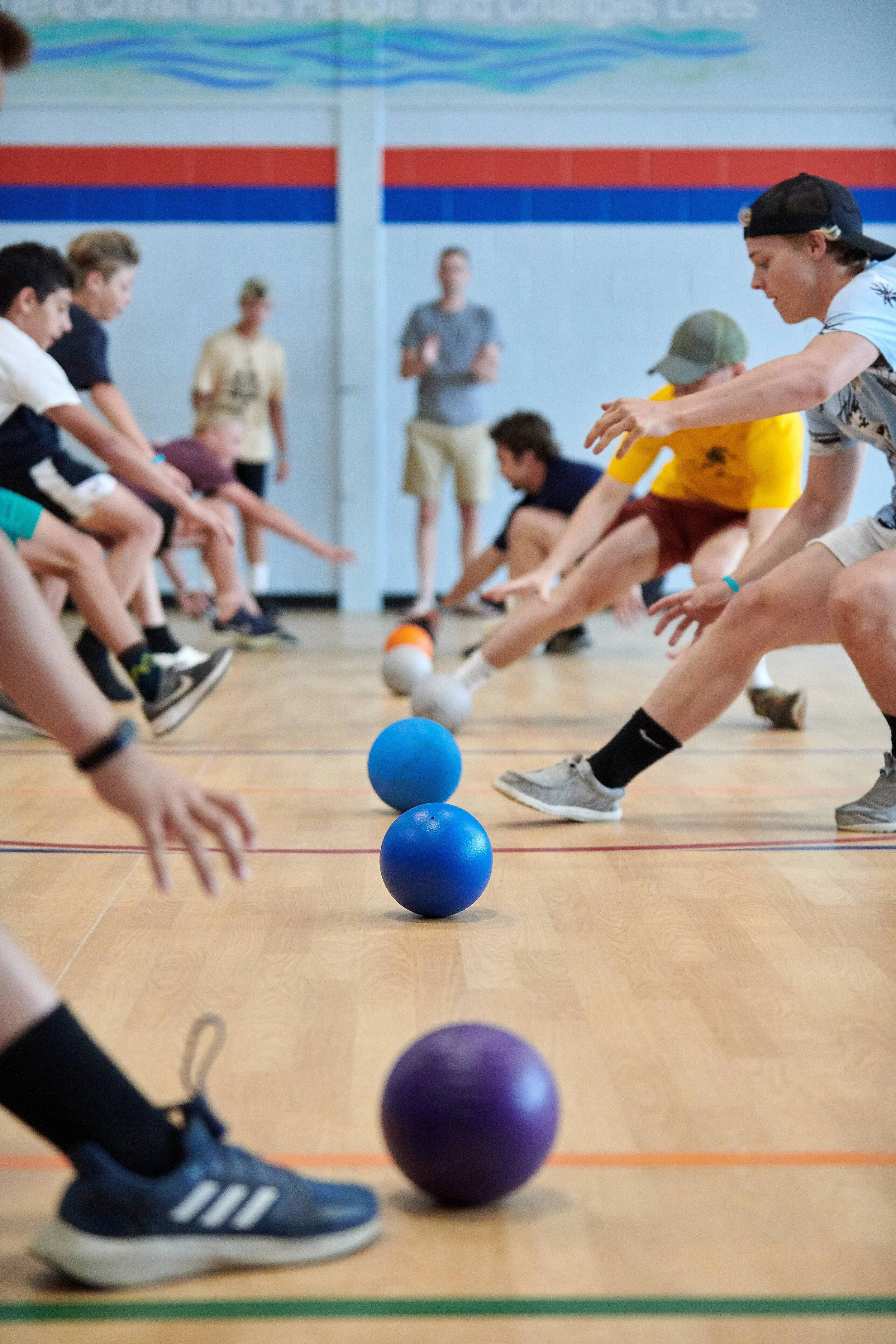 Children playing a game involving stretching and reaching for colorful balls in a gymnasium.