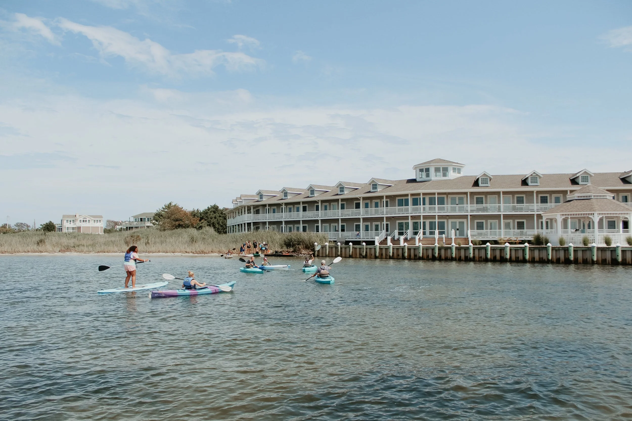 People paddleboarding on water in front of a large beachside building under a cloudy sky.
