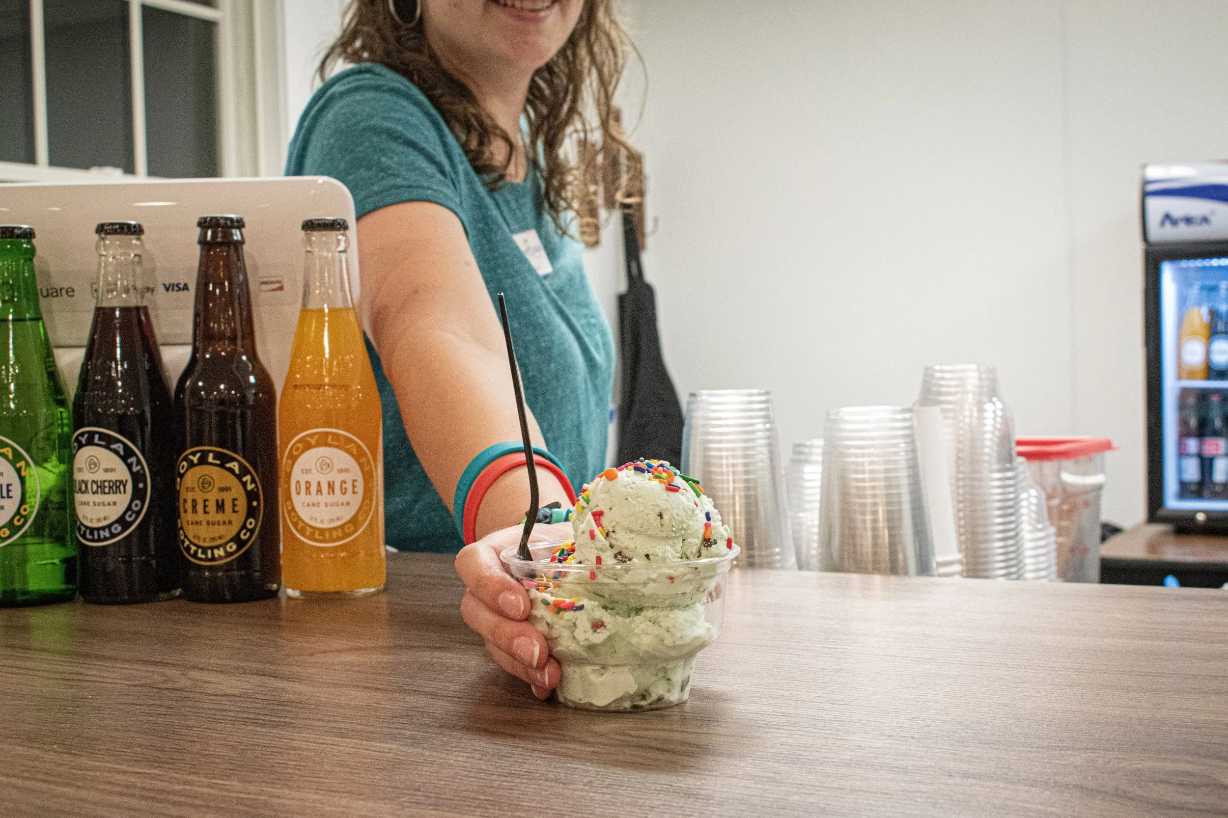 A woman behind a counter holding a cup of ice cream topped with colorful sprinkles