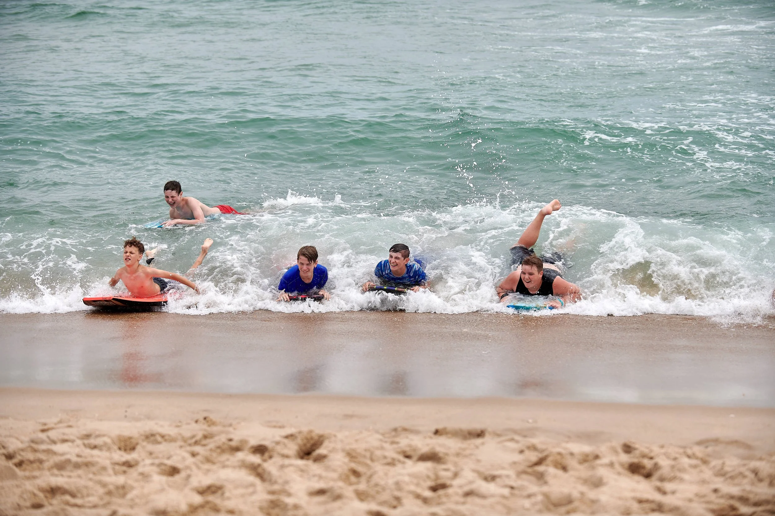 Five boys playing and swimming in the ocean near the sandy beach, having fun in the water.