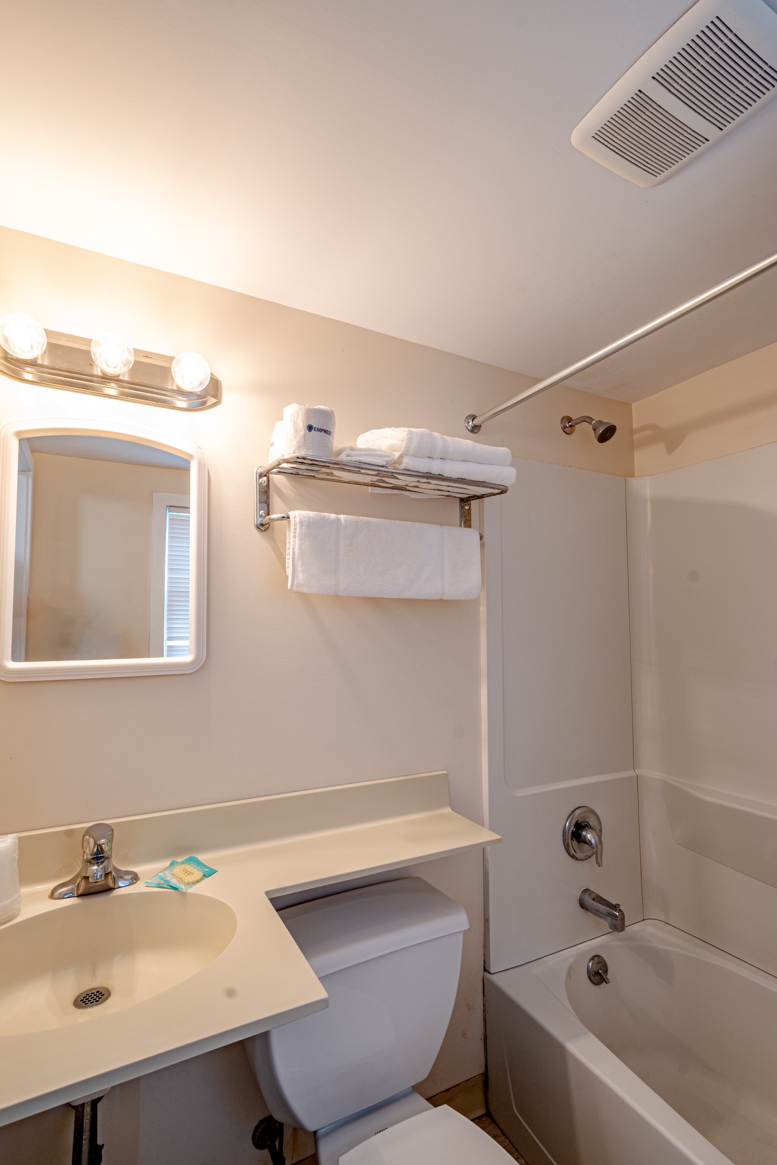 Bathroom with a sink, mirror, stack of towels, shower head, and bathtub in a small space.