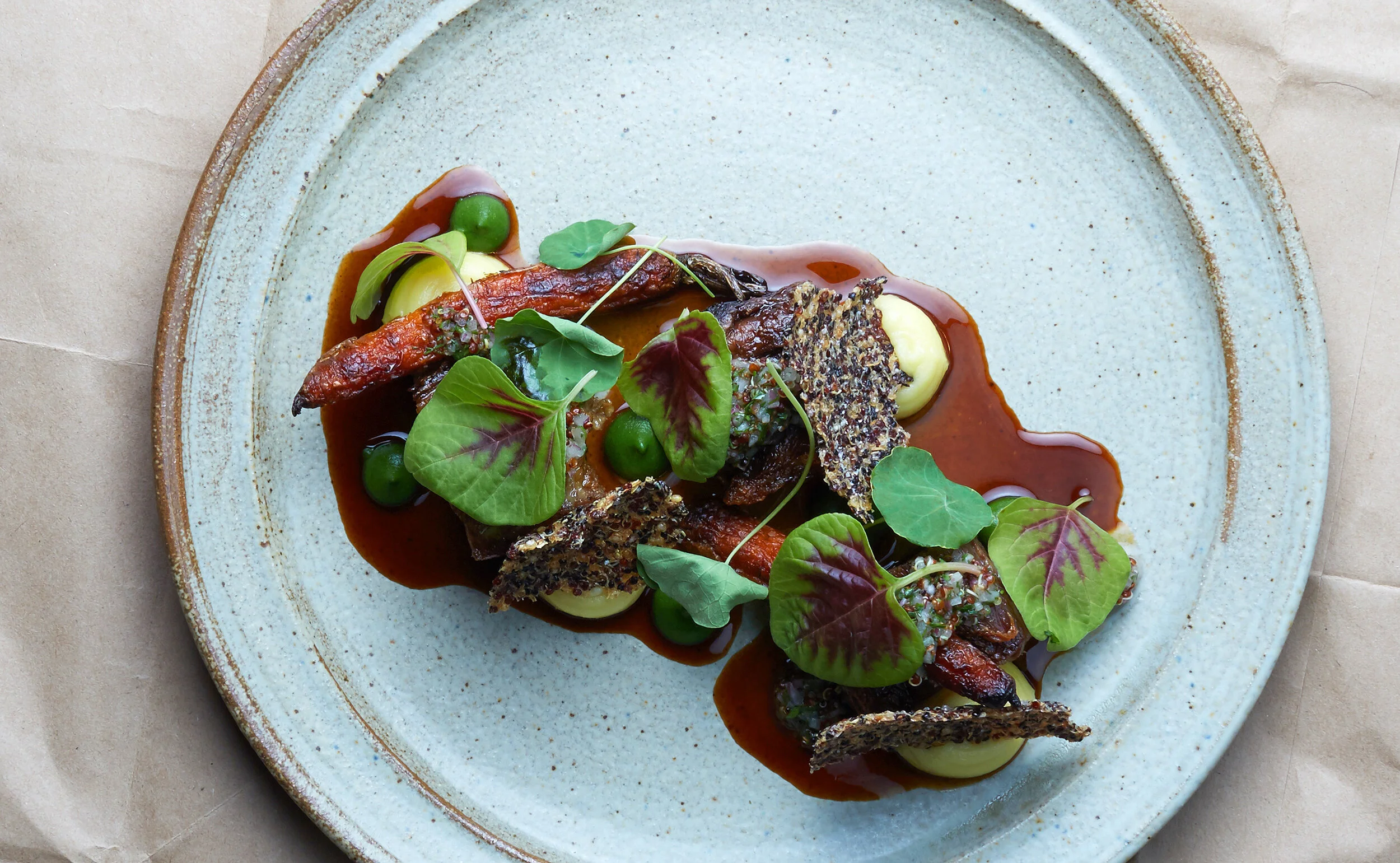 A gourmet dish with vegetables, crispy garnishes, and dark sauce on a light blue plate.