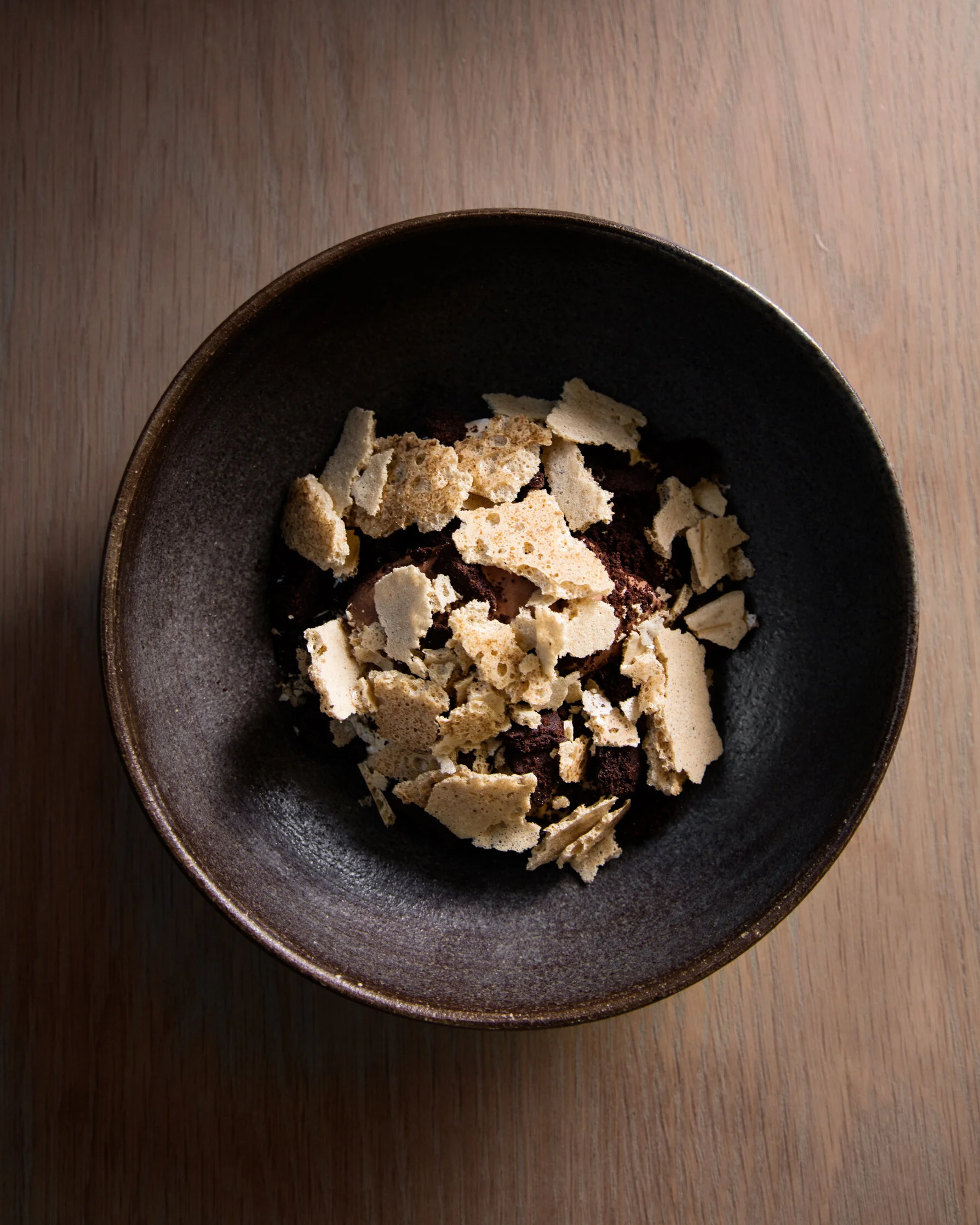 A top-down view of a black bowl with crushed cookies on a wooden surface.
