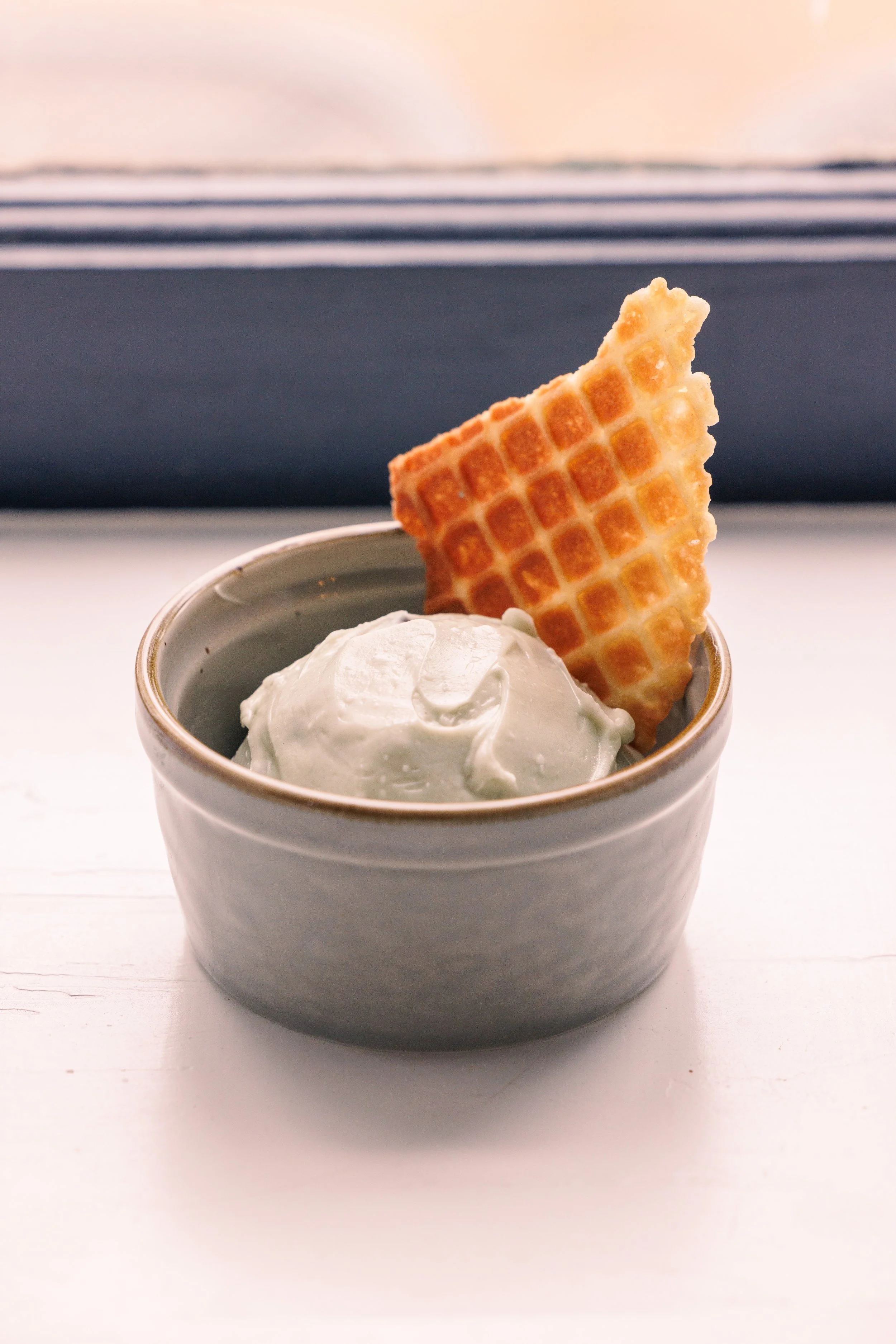 A scoop of ice cream with a waffle cone shard sticking out in a ramekin. 