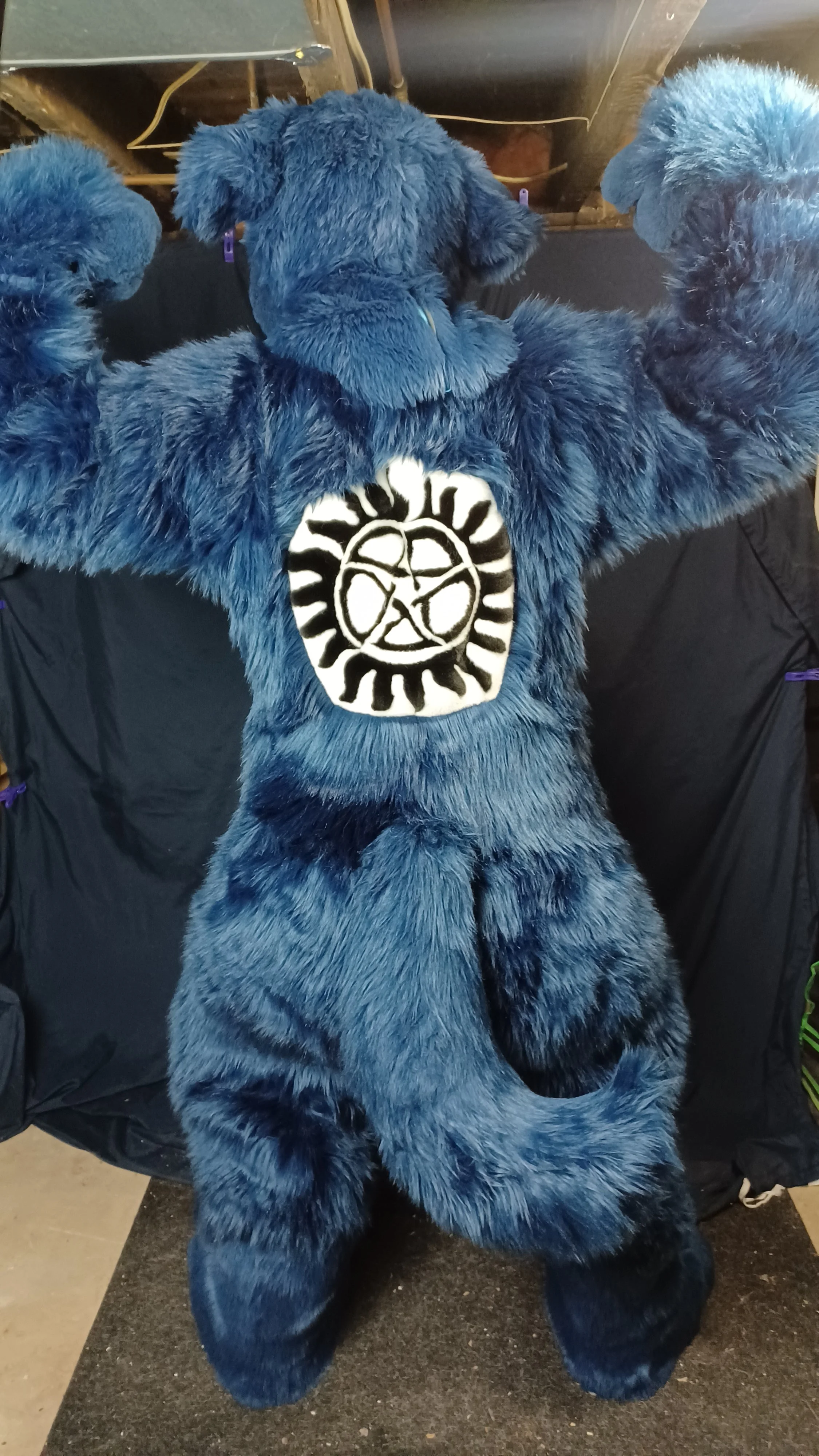 Blue furry costume with a black and white pentagram design on the back, resembling a mythical creature or animal, with the head and limbs made of plush material.