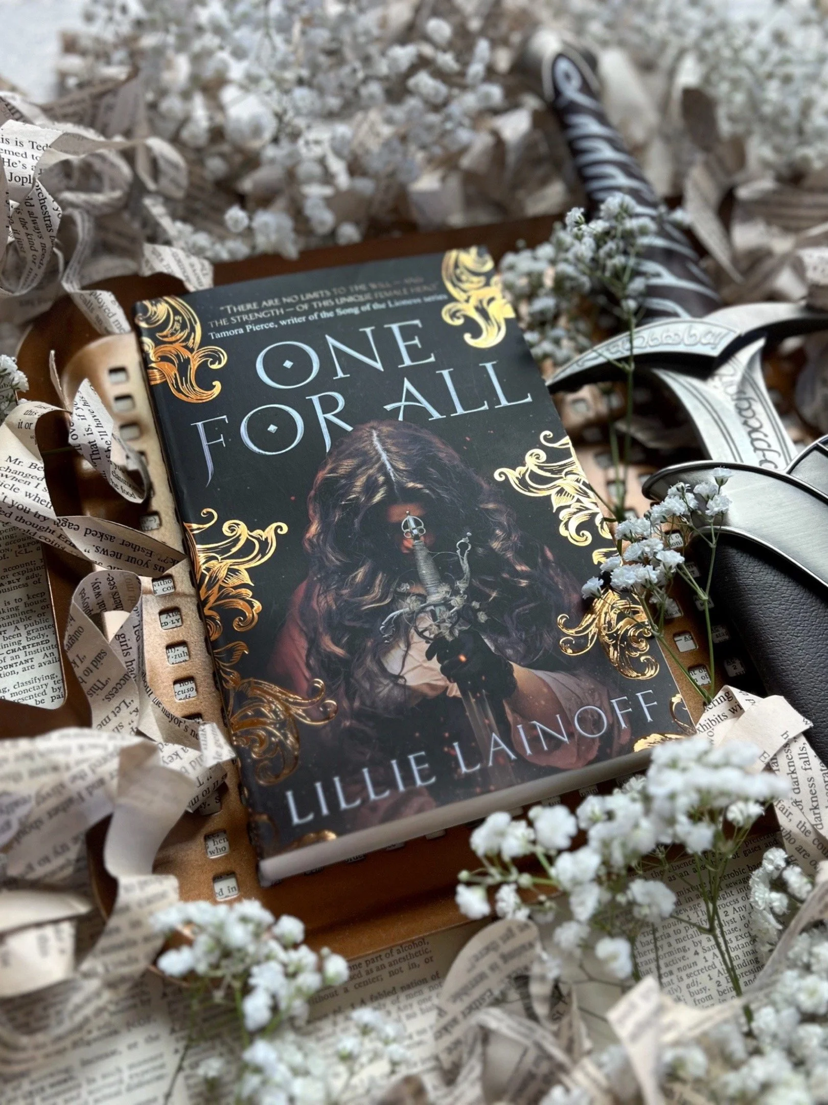 a dark brown book cover with an illustrated of a brown haired teen girl with her head bowed over a sword with silver decorative handle.