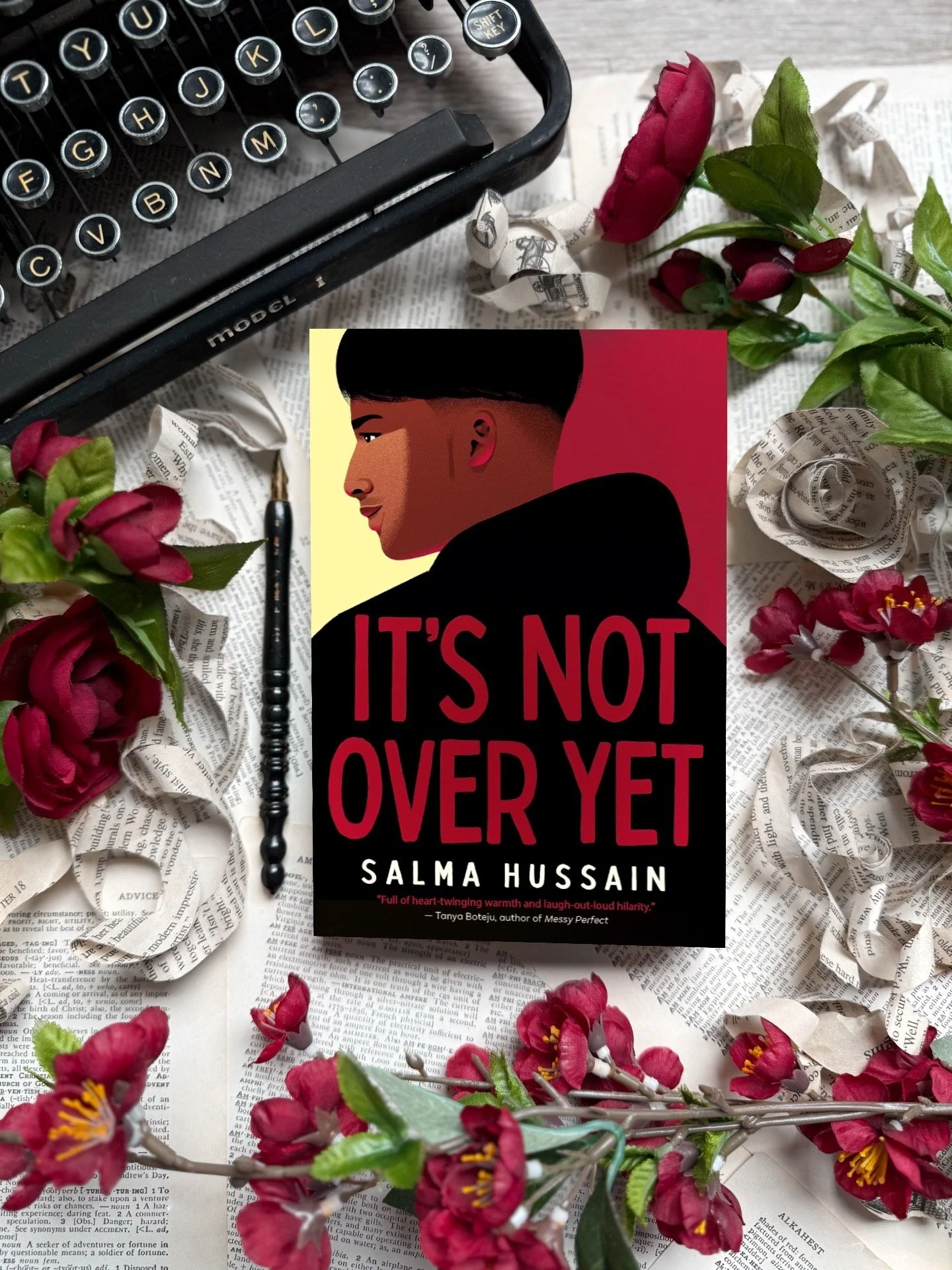 a book with an illustration of a brown teen boy in silhouette with “It’s Not Over Yet” and “Salma Hussain” written in bold red and white text. The teen wears a black hoodie and is framed by red and yellow.