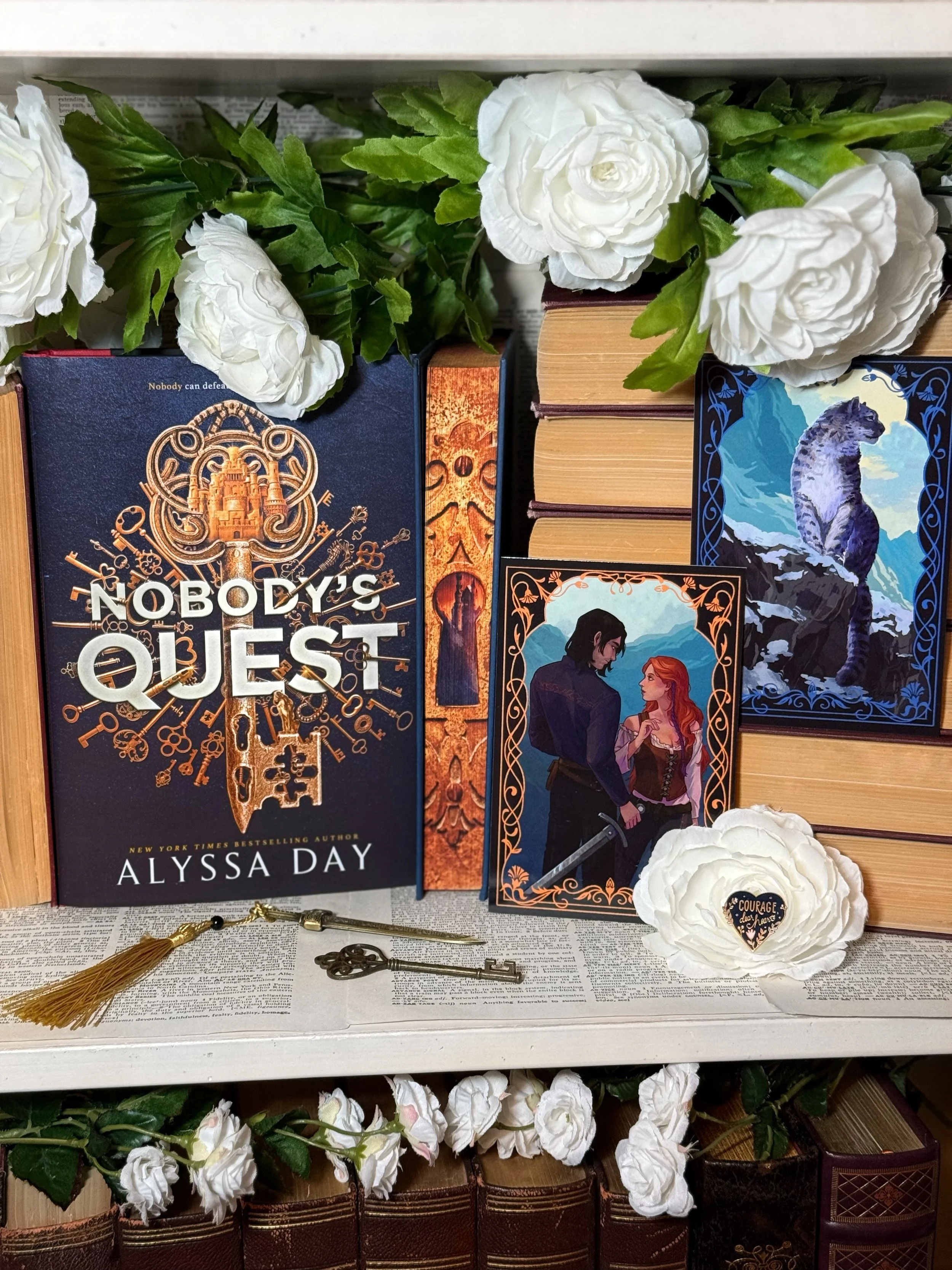 a black book with an illustration of a circle of ornate gold keys with “Nobody’s Quest” written in bold white text in the center. The book sits on a white shelf around a stack of books with their edges showing.