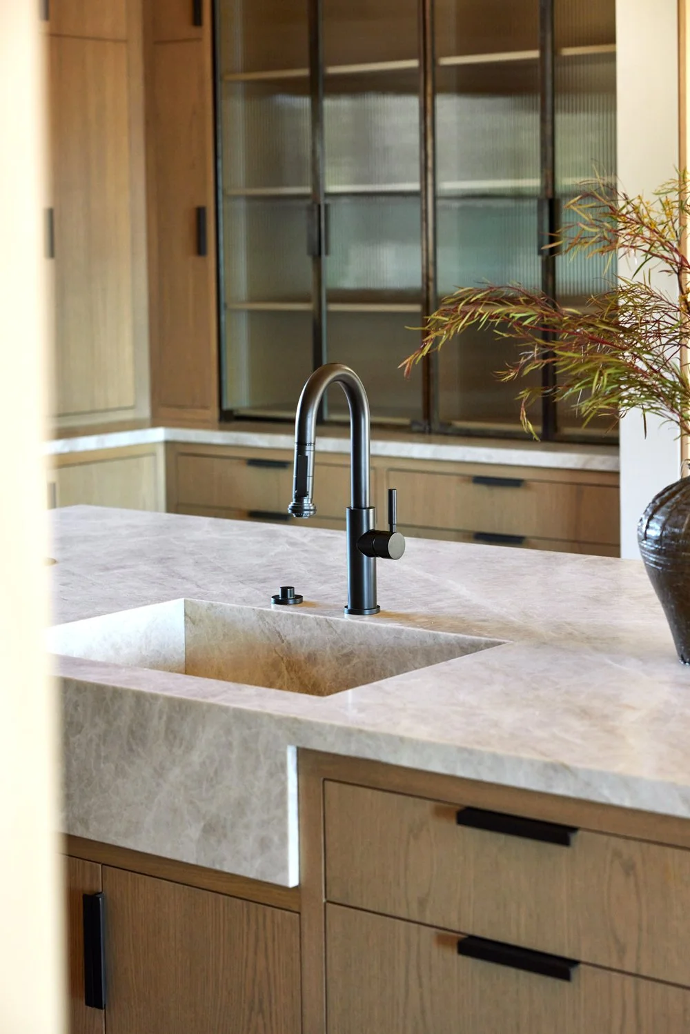 Modern kitchen with a black faucet, beige marble sink, wooden cabinets, and a potted plant.