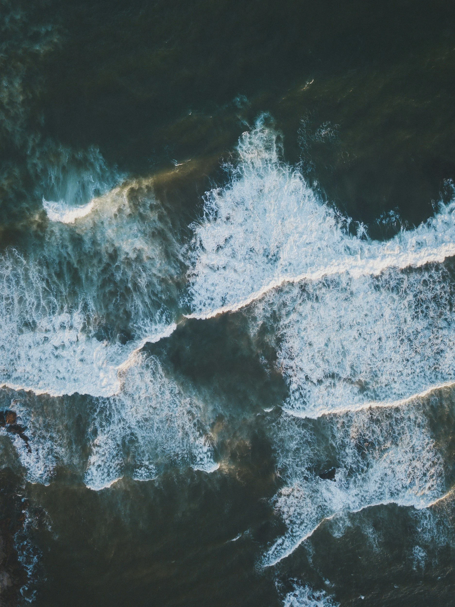 Aerial view of ocean waves crashing against each other with white foam and dark water.