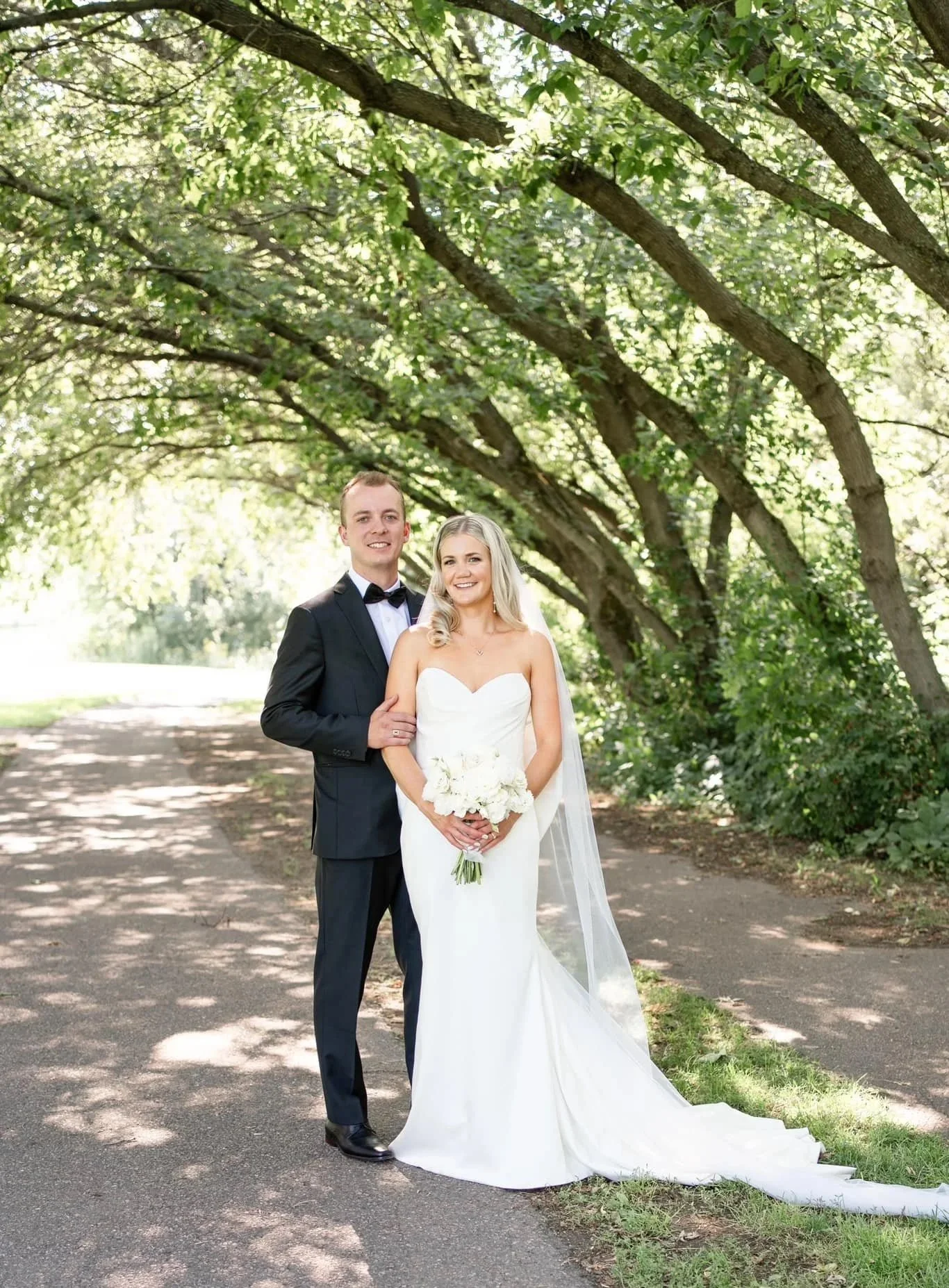 A bride and groom kiss during their outdoor wedding ceremony surrounded by friends and family.