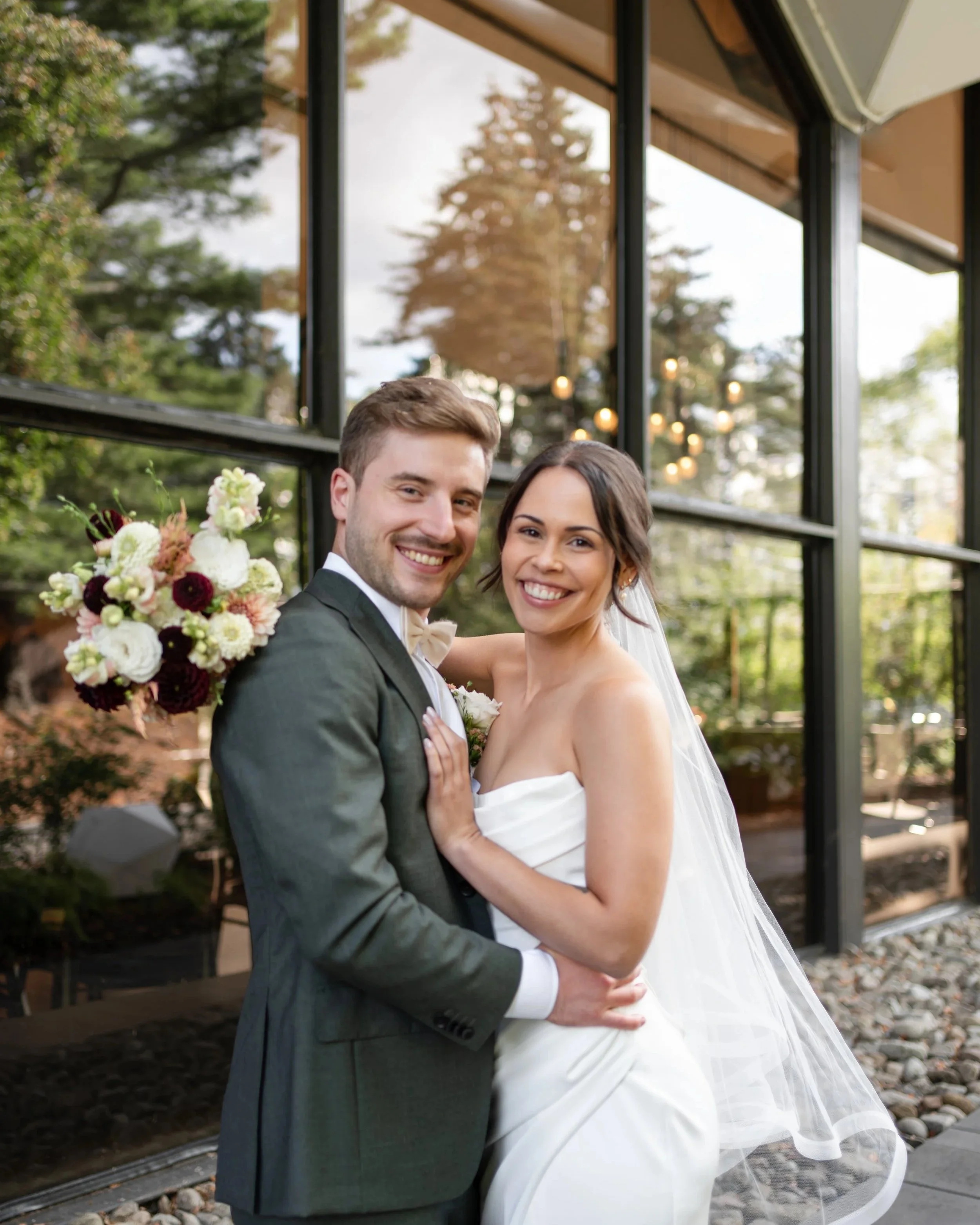 A happy bride and groom smiling in front of modern building with large glass windows. La Toundra, Montreal